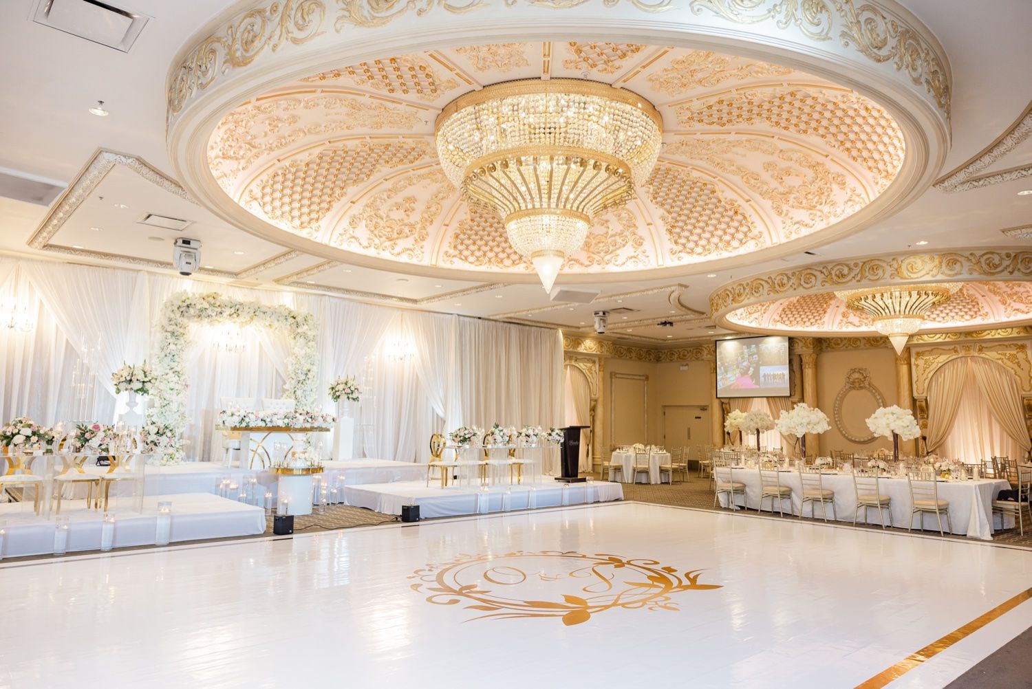 Luxury ballroom with elegant crystal chandeliers, ornate ceiling details, and white dance floor featuring gold monogram design.