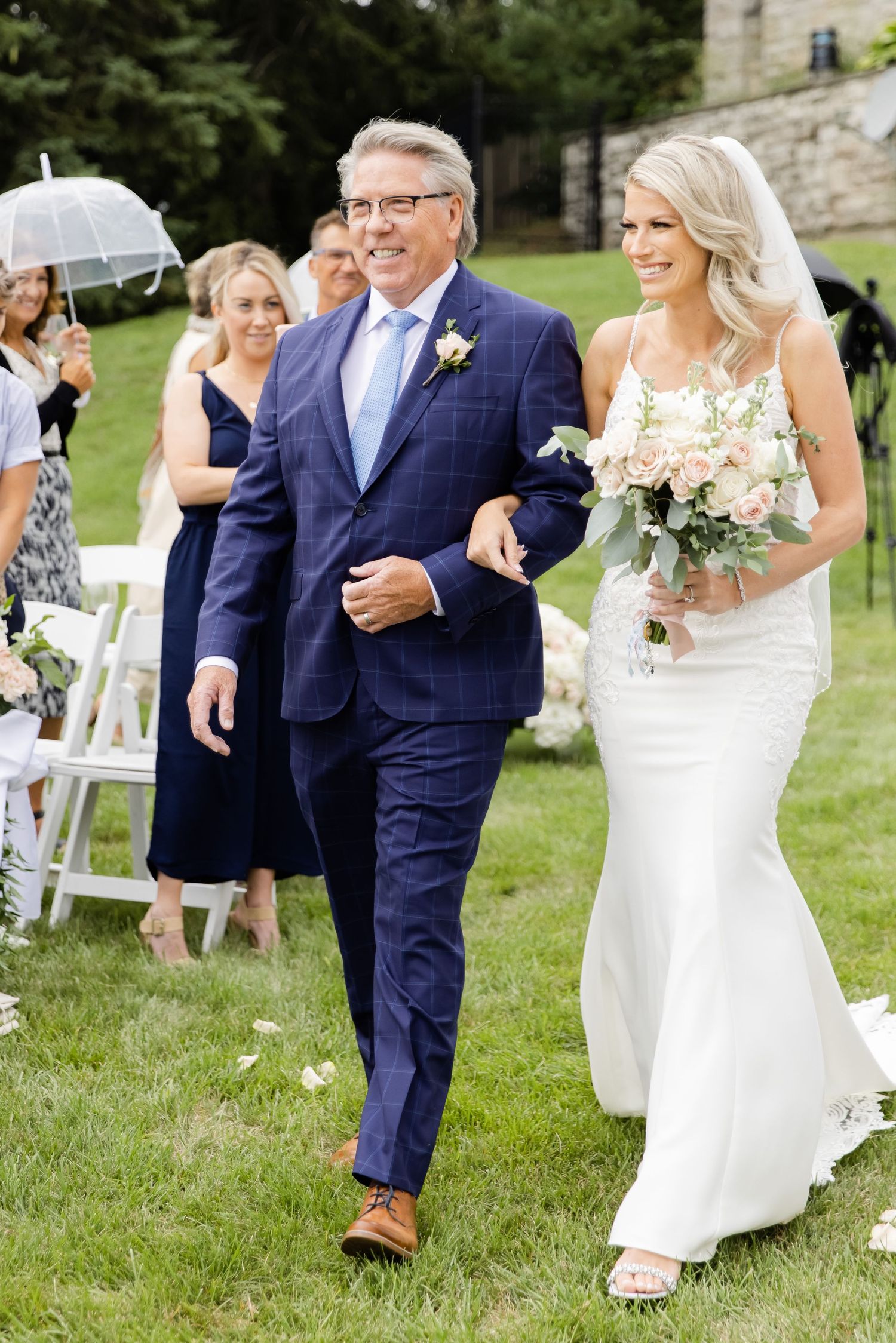 Joyful wedding procession walking down outdoor aisle with white chairs and floral arrangements.