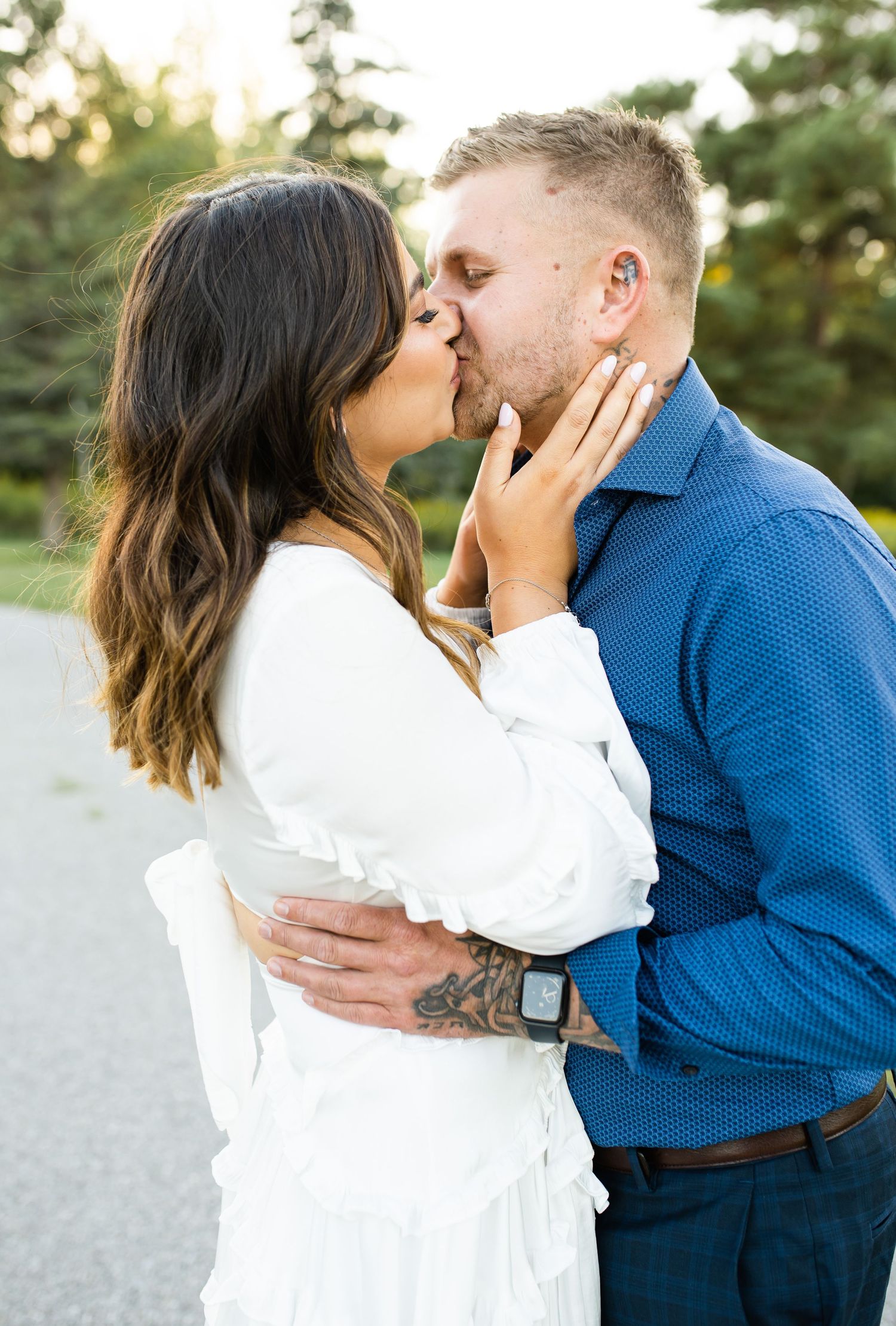 Tender embrace between couple in coordinated white and blue outfits on nature path.
