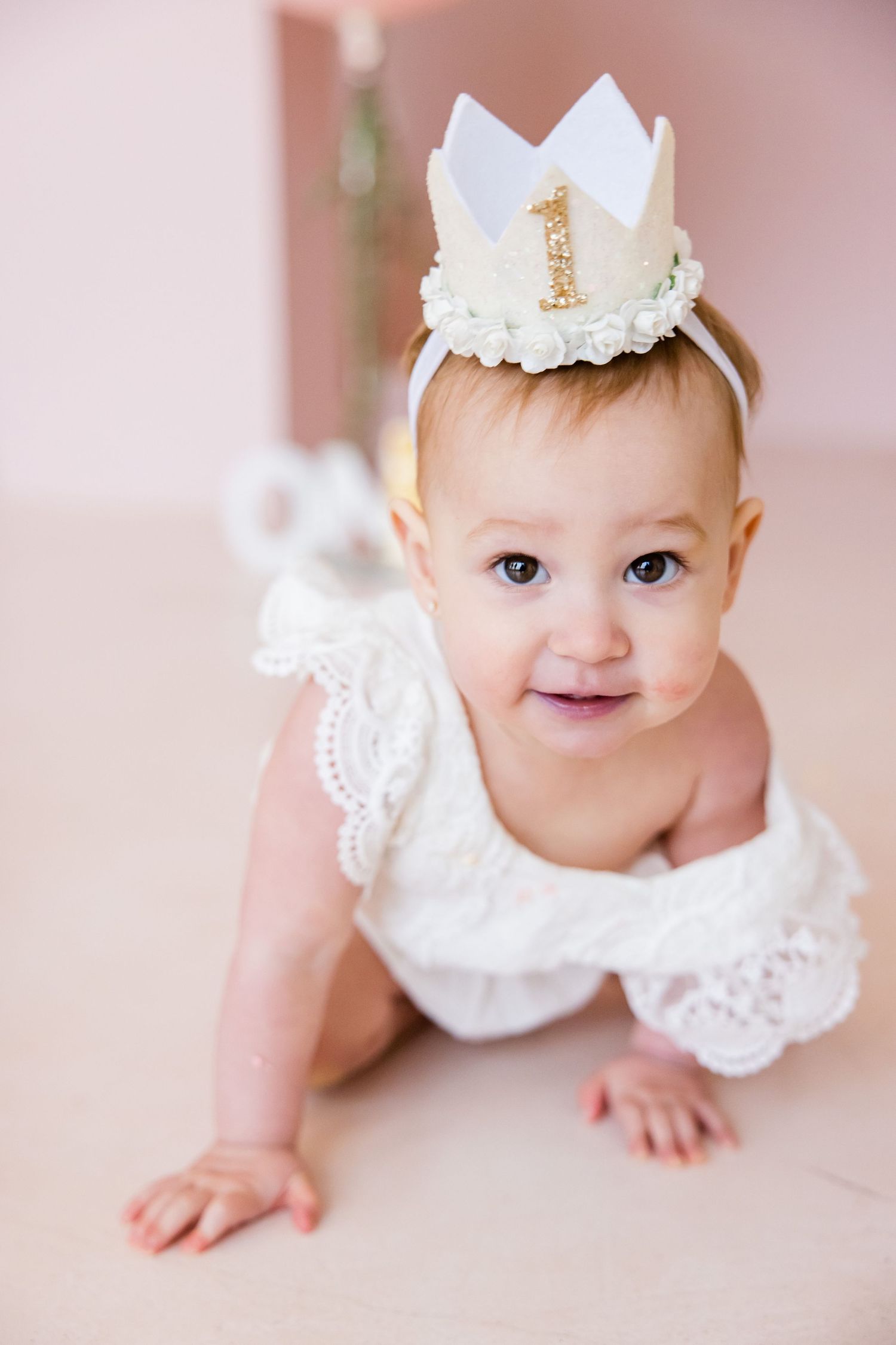 Overhead shot of baby in white lace dress wearing decorative birthday crown.