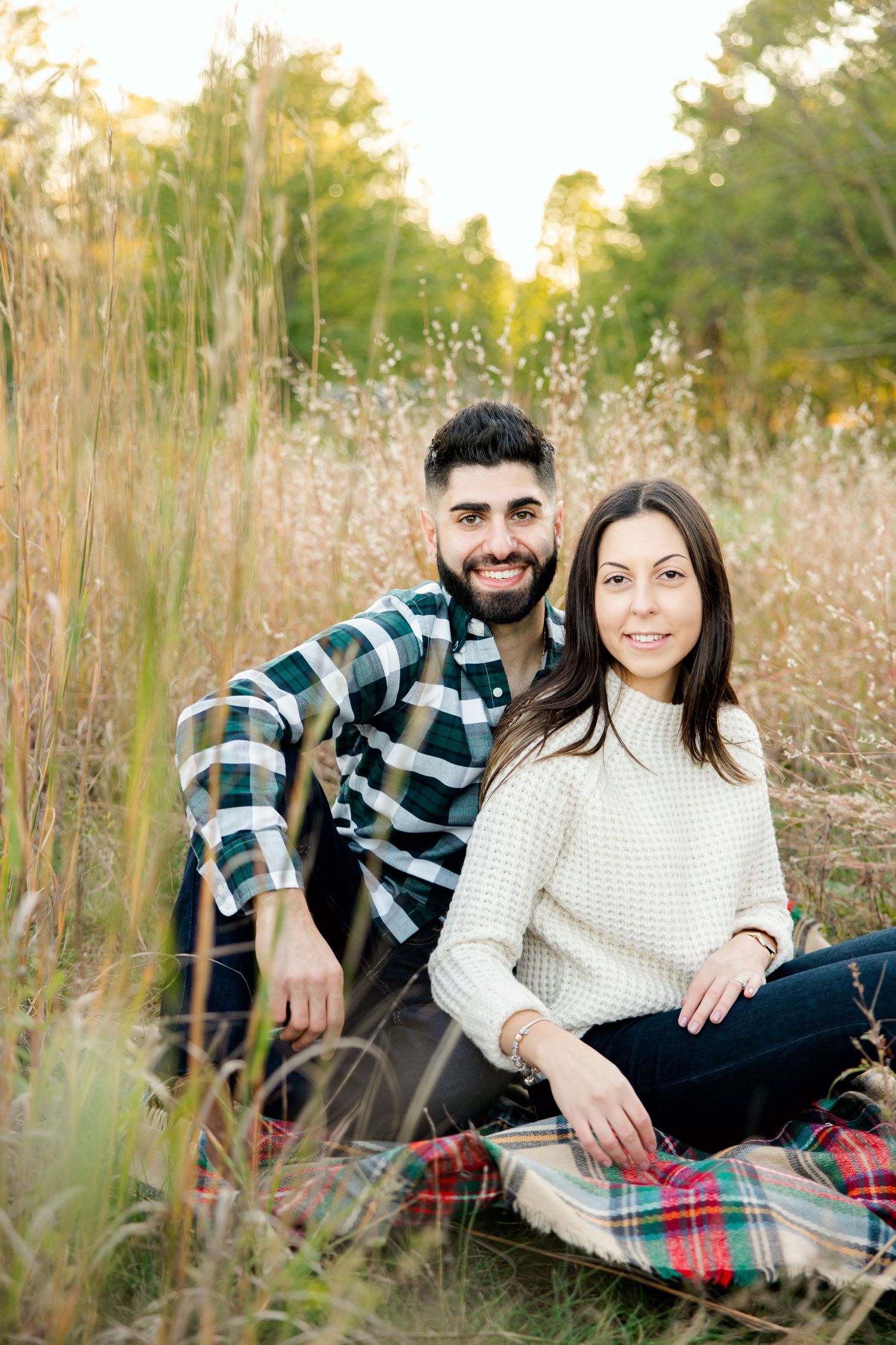 Romantic outdoor portrait of couple sitting on plaid blanket surrounded by tall golden grass.