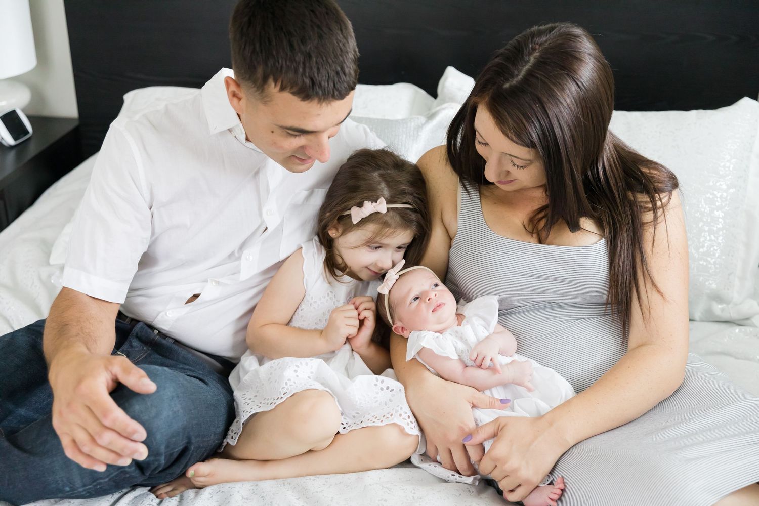 Family of four sitting together on bed with newborn baby.