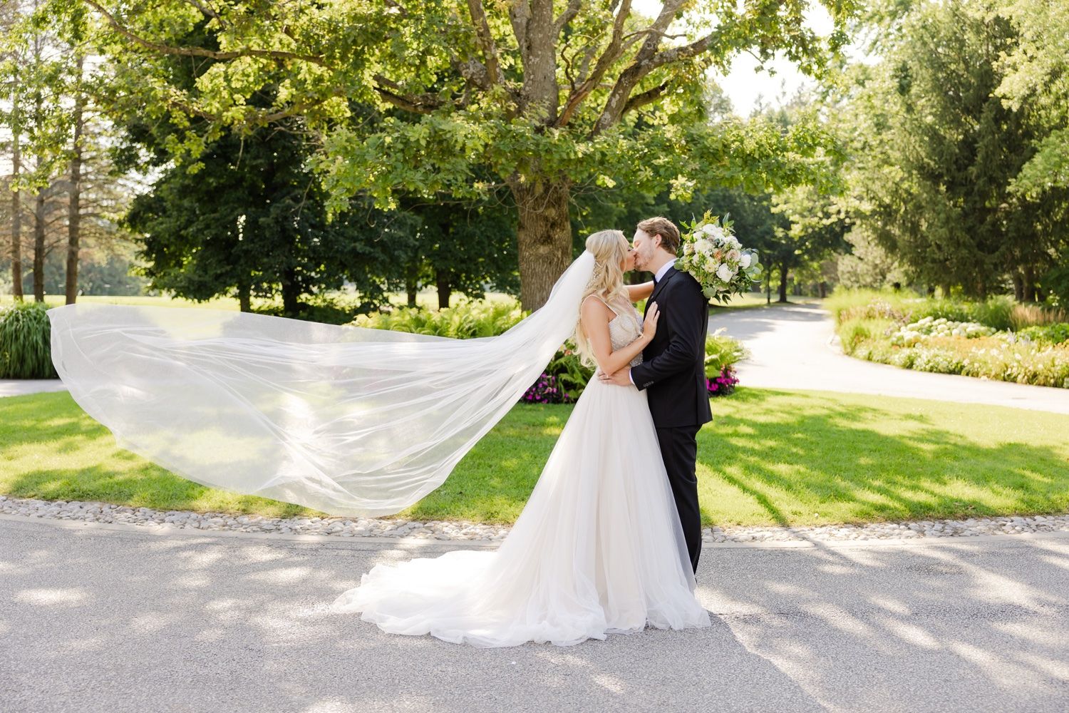 Romantic wedding portrait with bride's veil flowing in the breeze on a garden path.