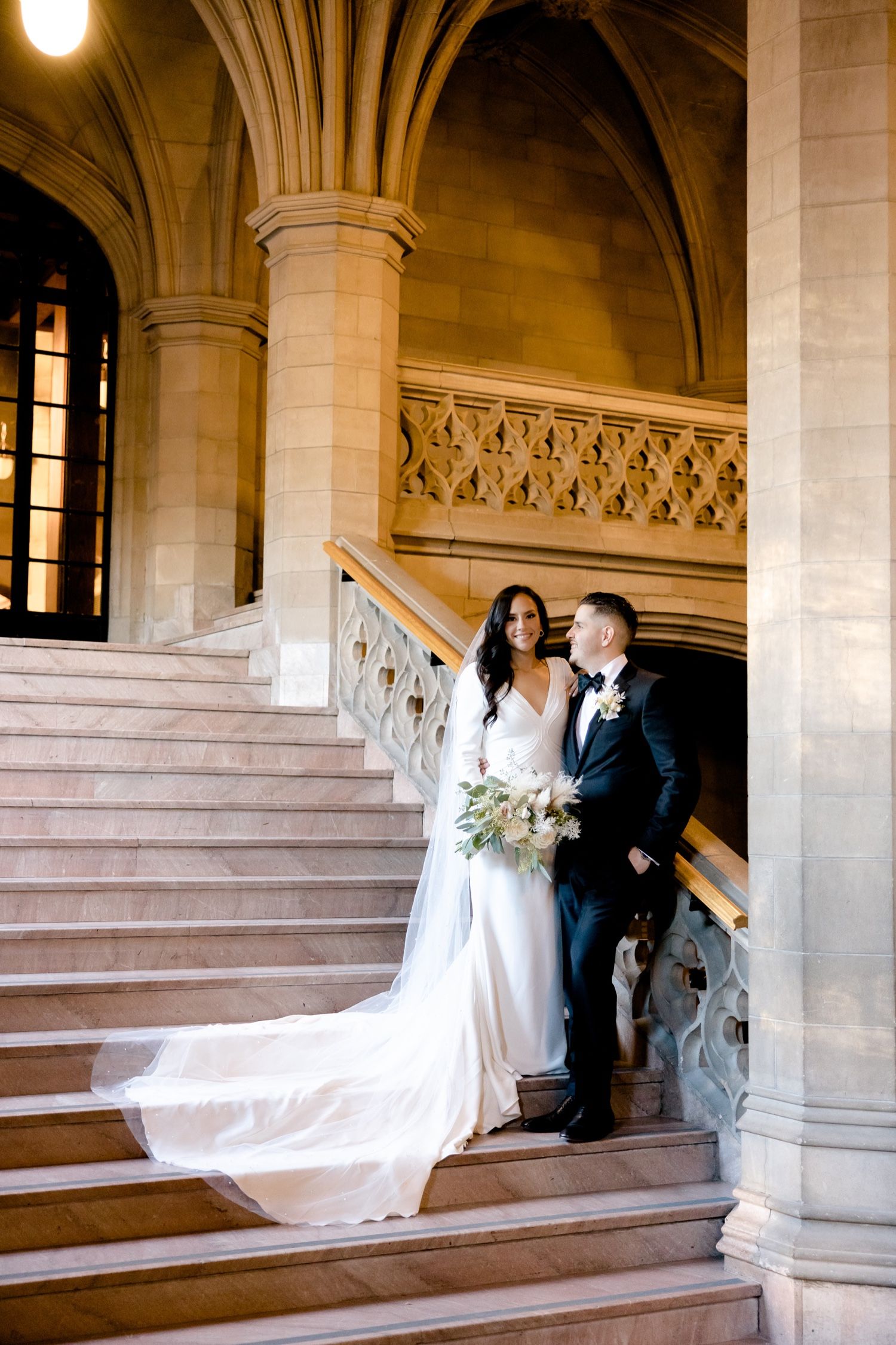 A couple shares an intimate moment on an elegant stone staircase with Gothic architectural details.