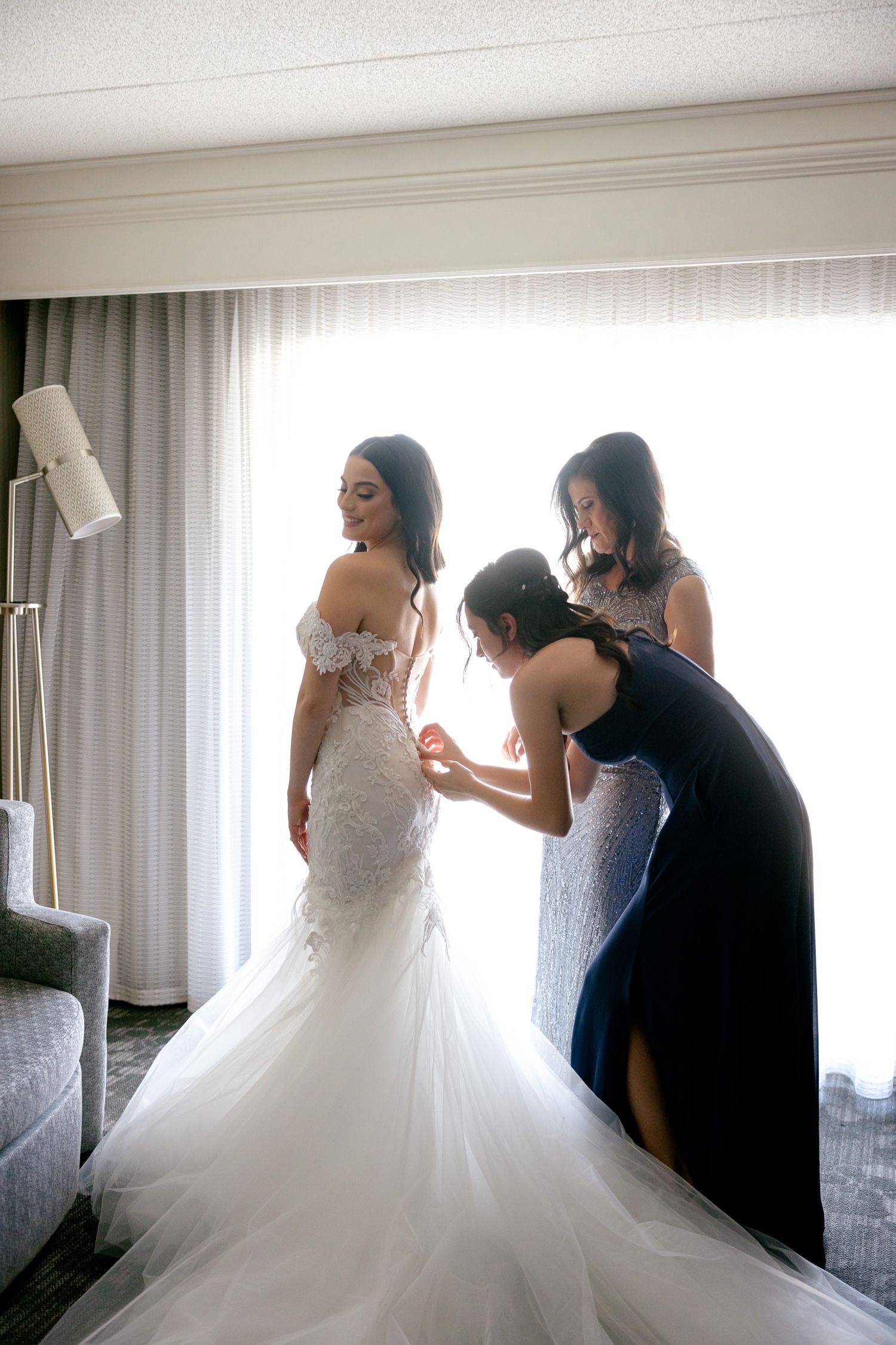 Wedding dress preparation with detailed lace and flowing train in hotel room.