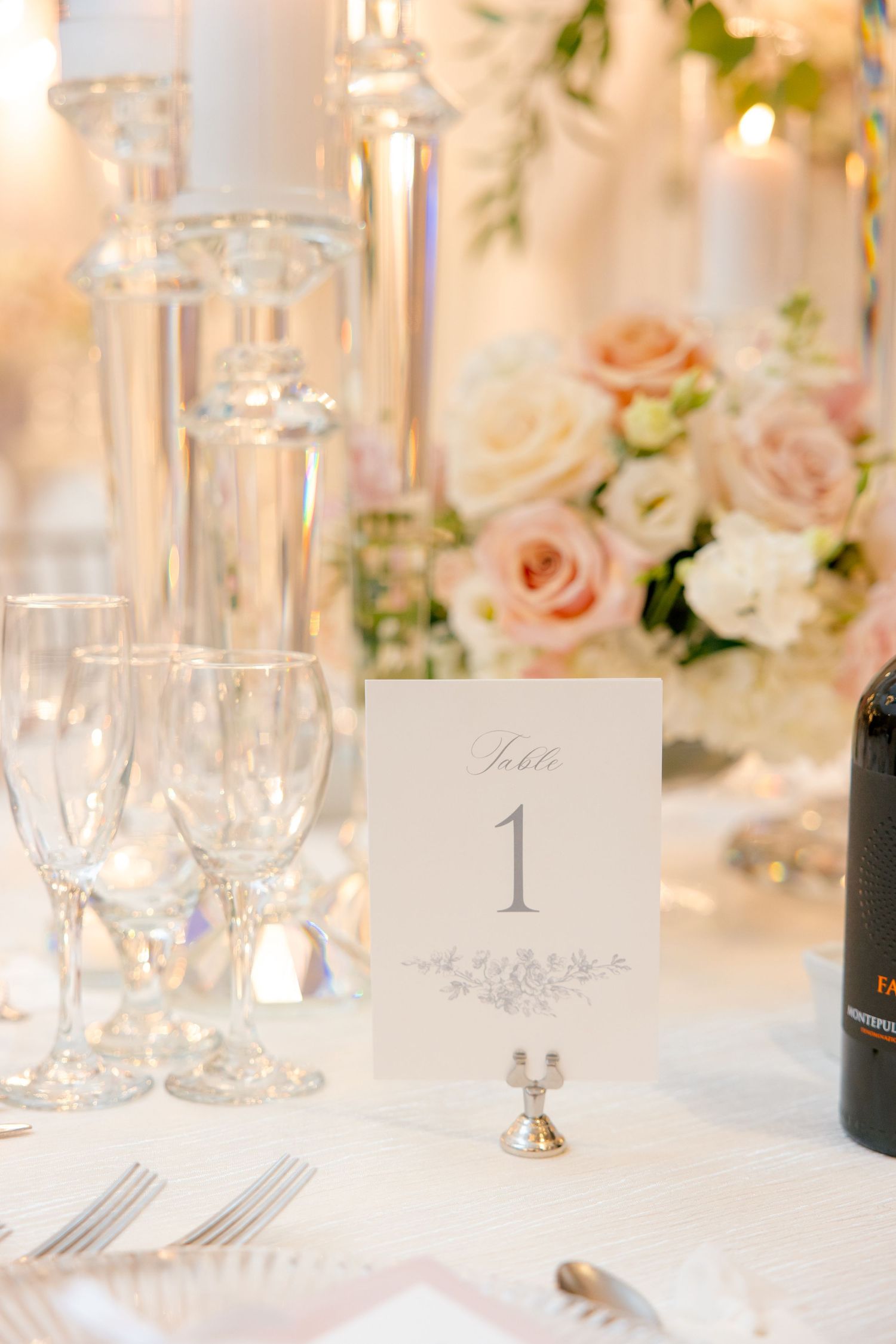 Elegant table number display with crystal glassware and soft floral arrangements at wedding reception.