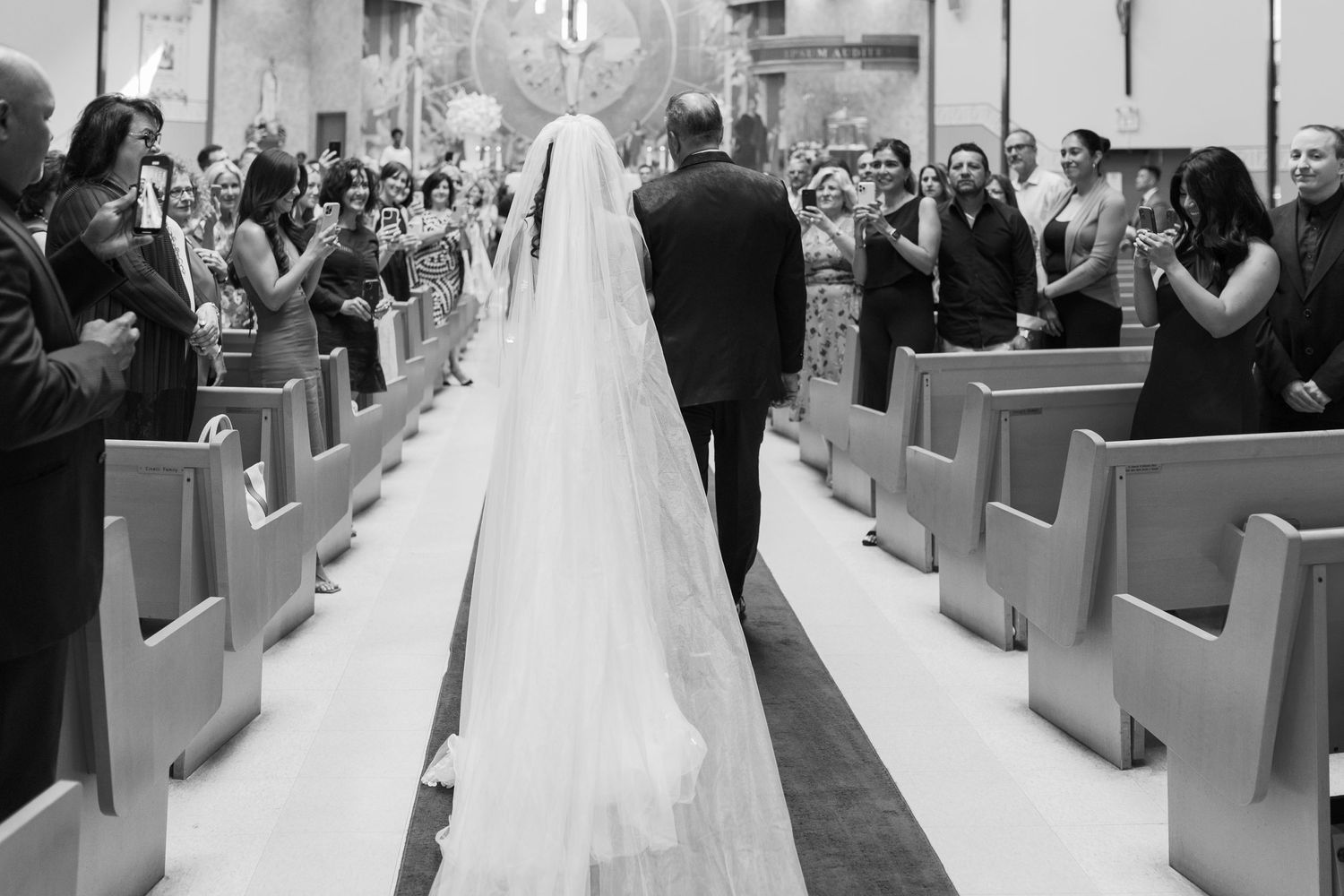 Black and white photo of wedding ceremony with couple walking down church aisle.