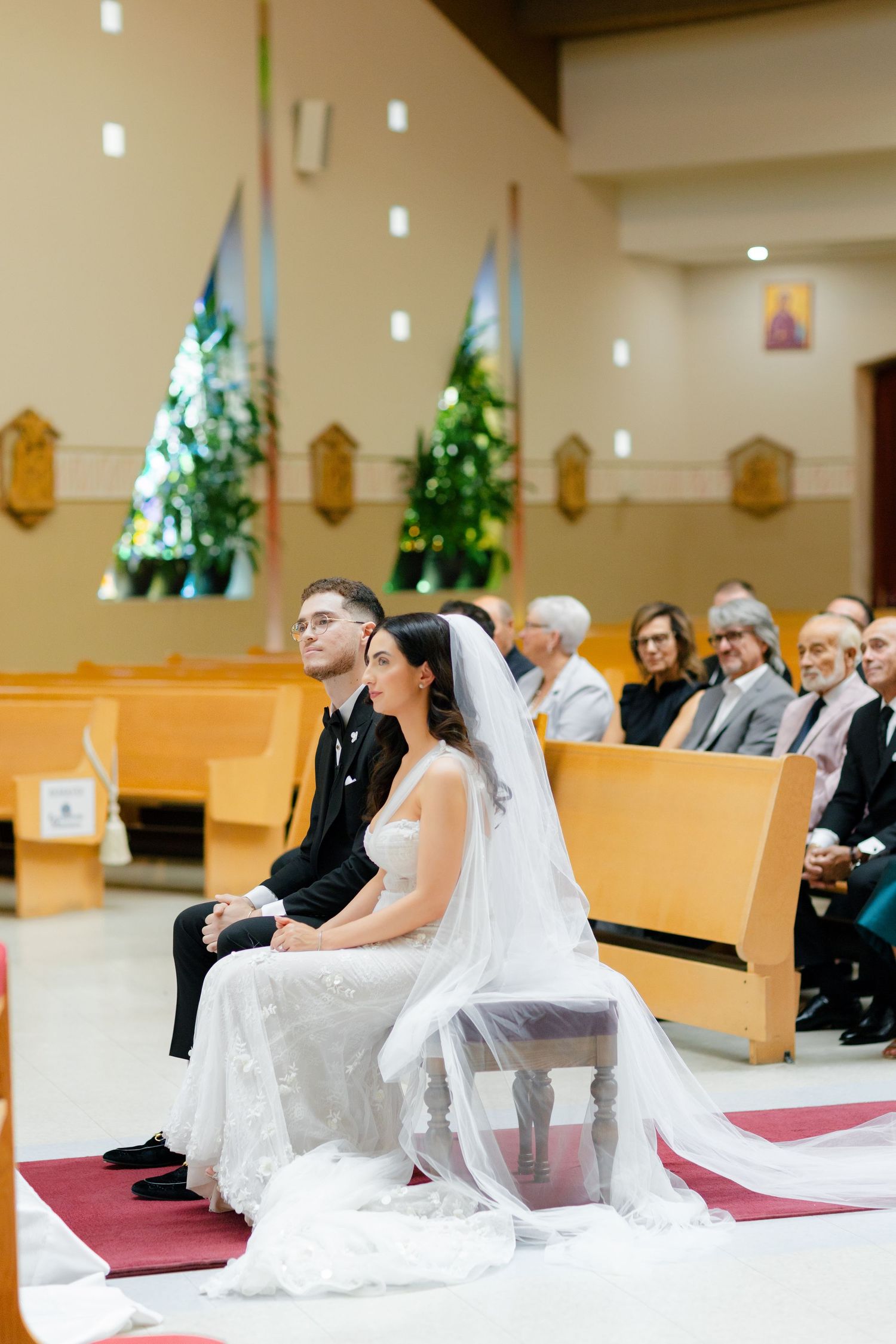 Newlyweds seated in church pews during their wedding ceremony with family looking on.