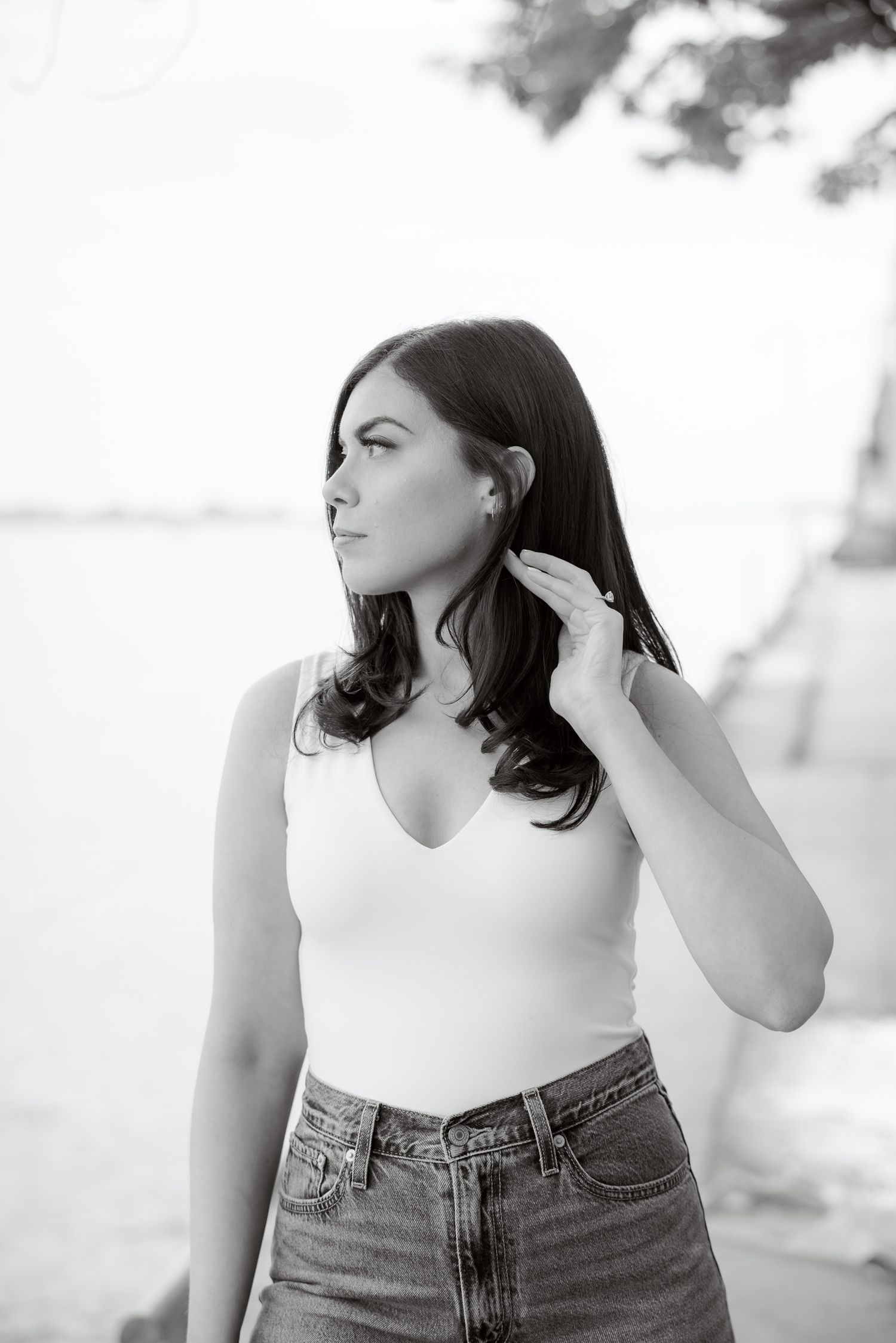 Black and white portrait of person in white top looking to side by waterfront.