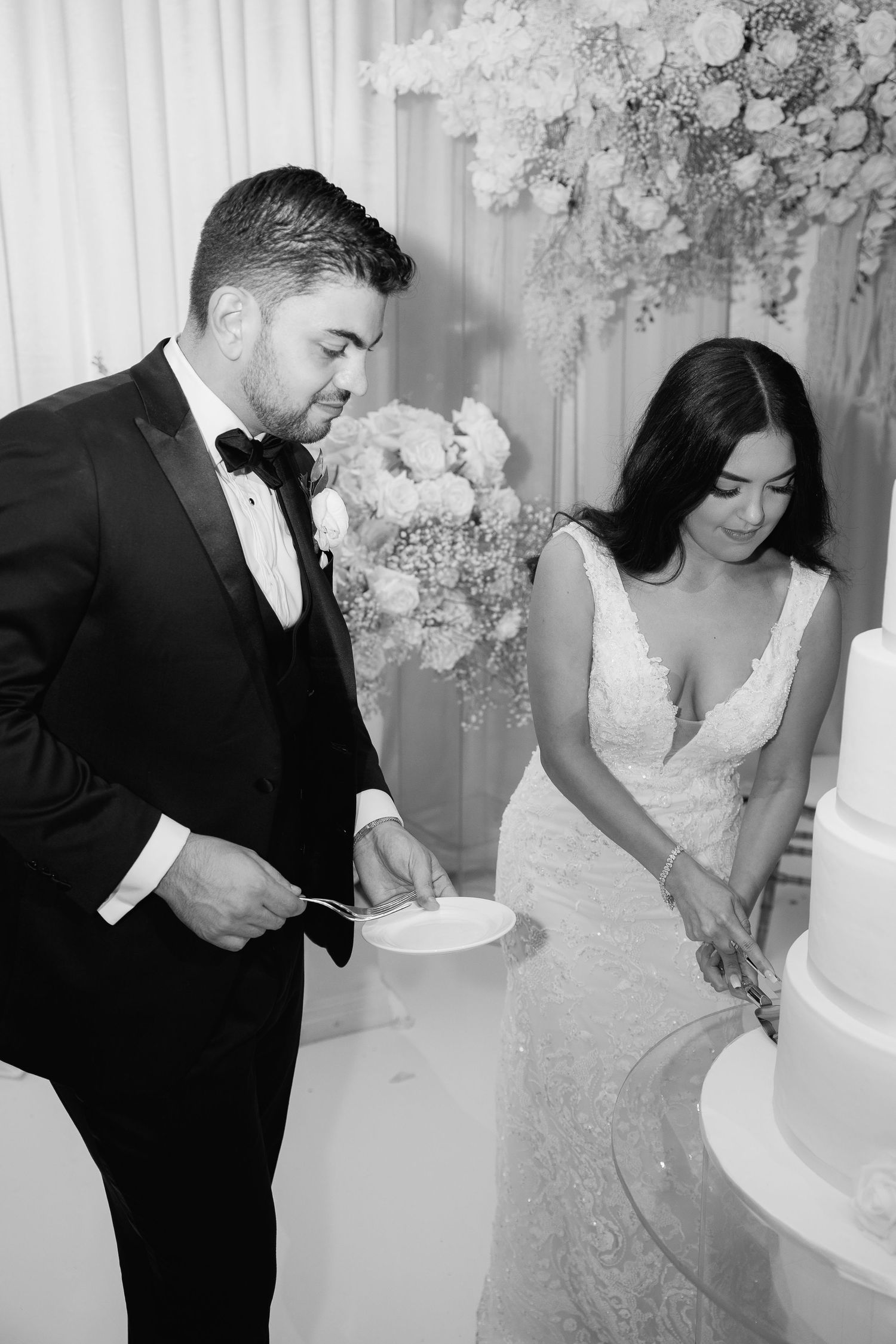 Black and white photo of couple cutting their elegant white wedding cake.