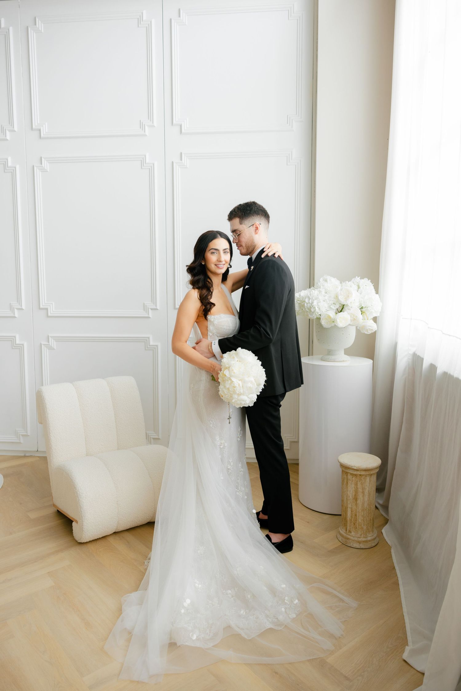 A full-length wedding portrait showing a couple in black and white attire against a minimalist backdrop.