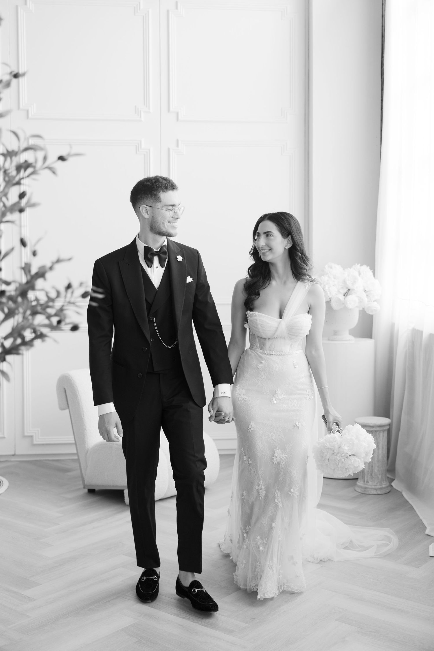 Black and white photo of a wedding couple walking hand in hand in an elegant interior space.