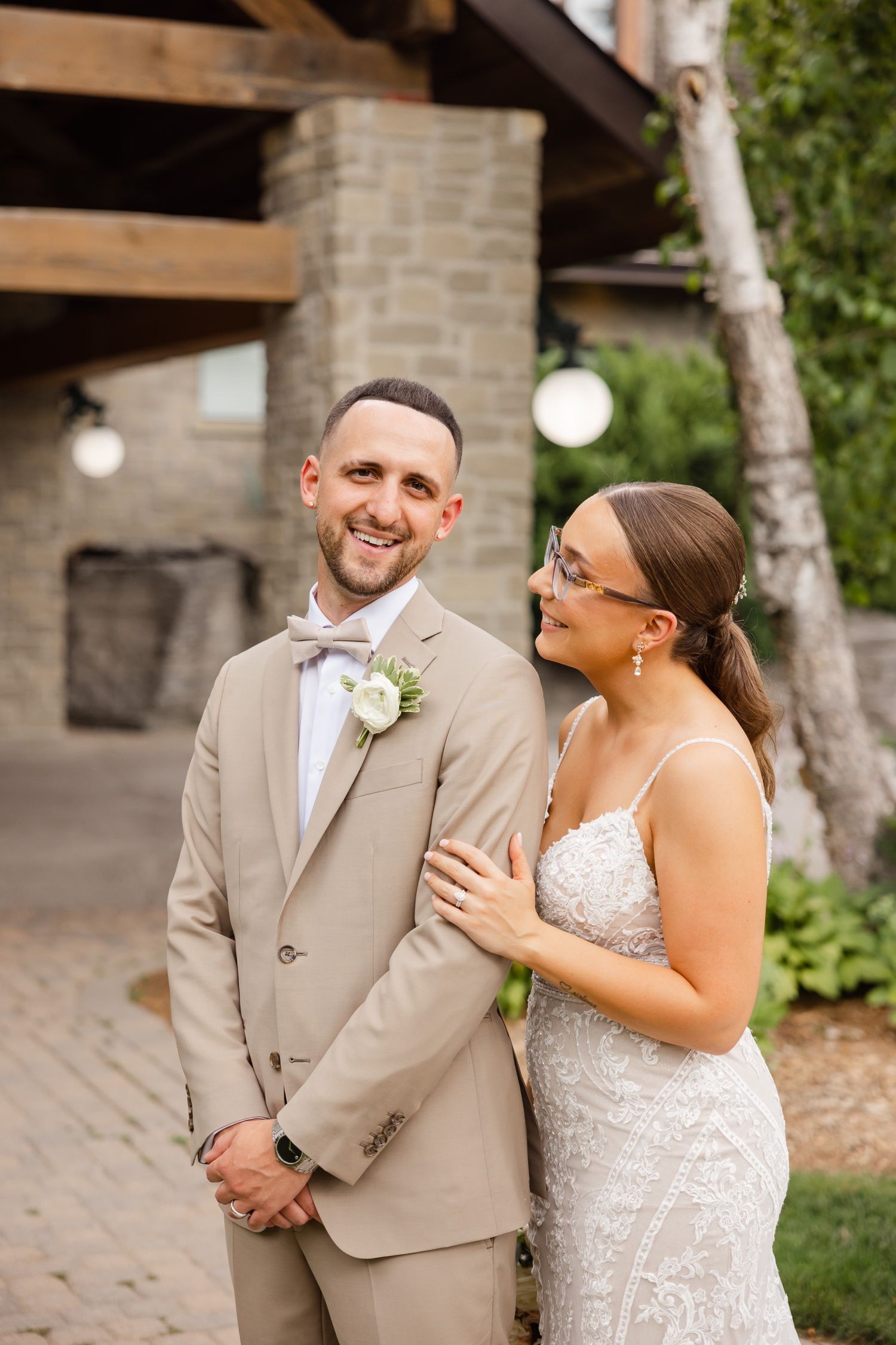 A couple shares a joyful moment during their outdoor wedding, wearing beige suit and lace gown.