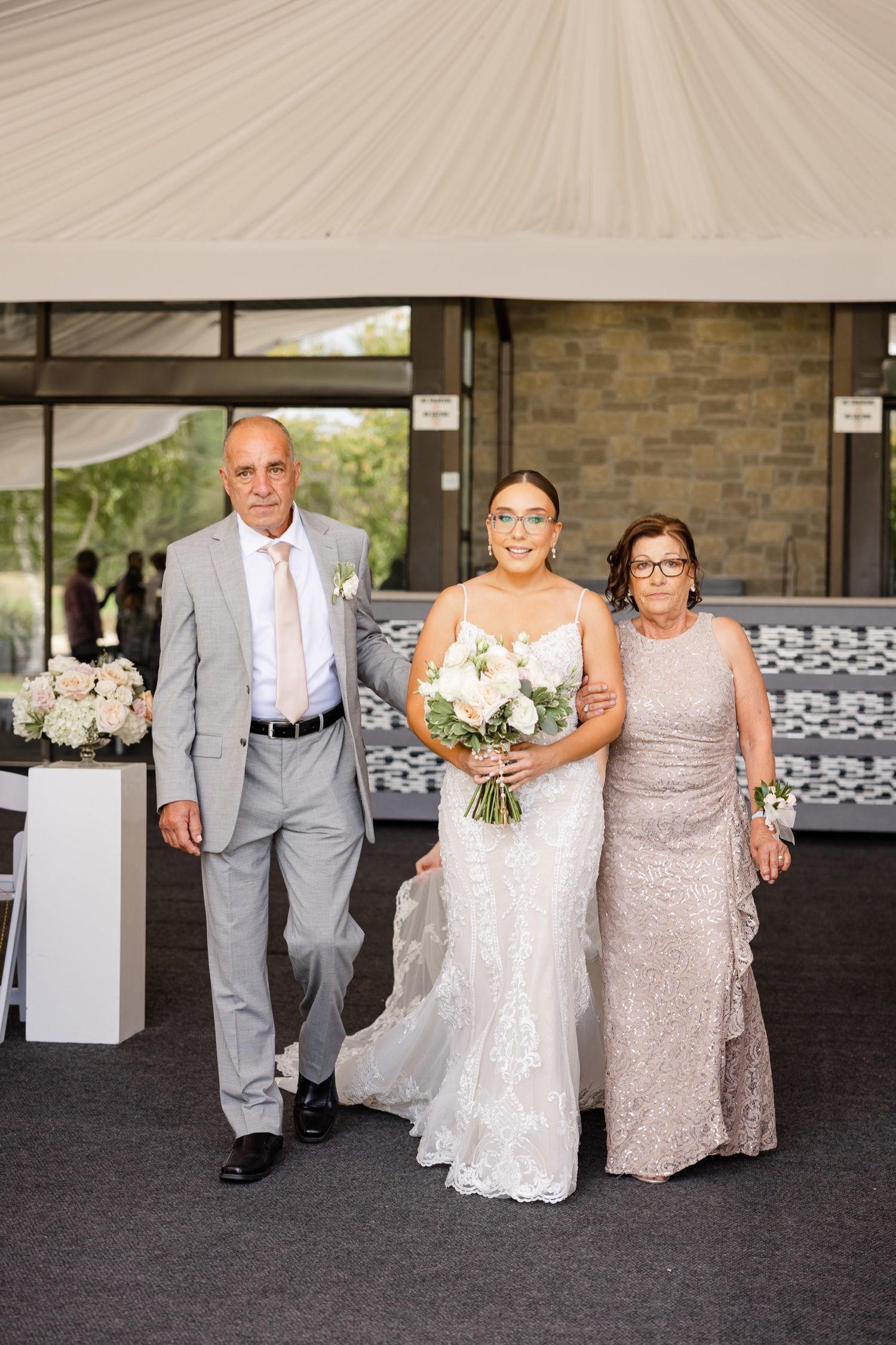 An elegant wedding processional moment under a draped tent entrance with stone wall details.