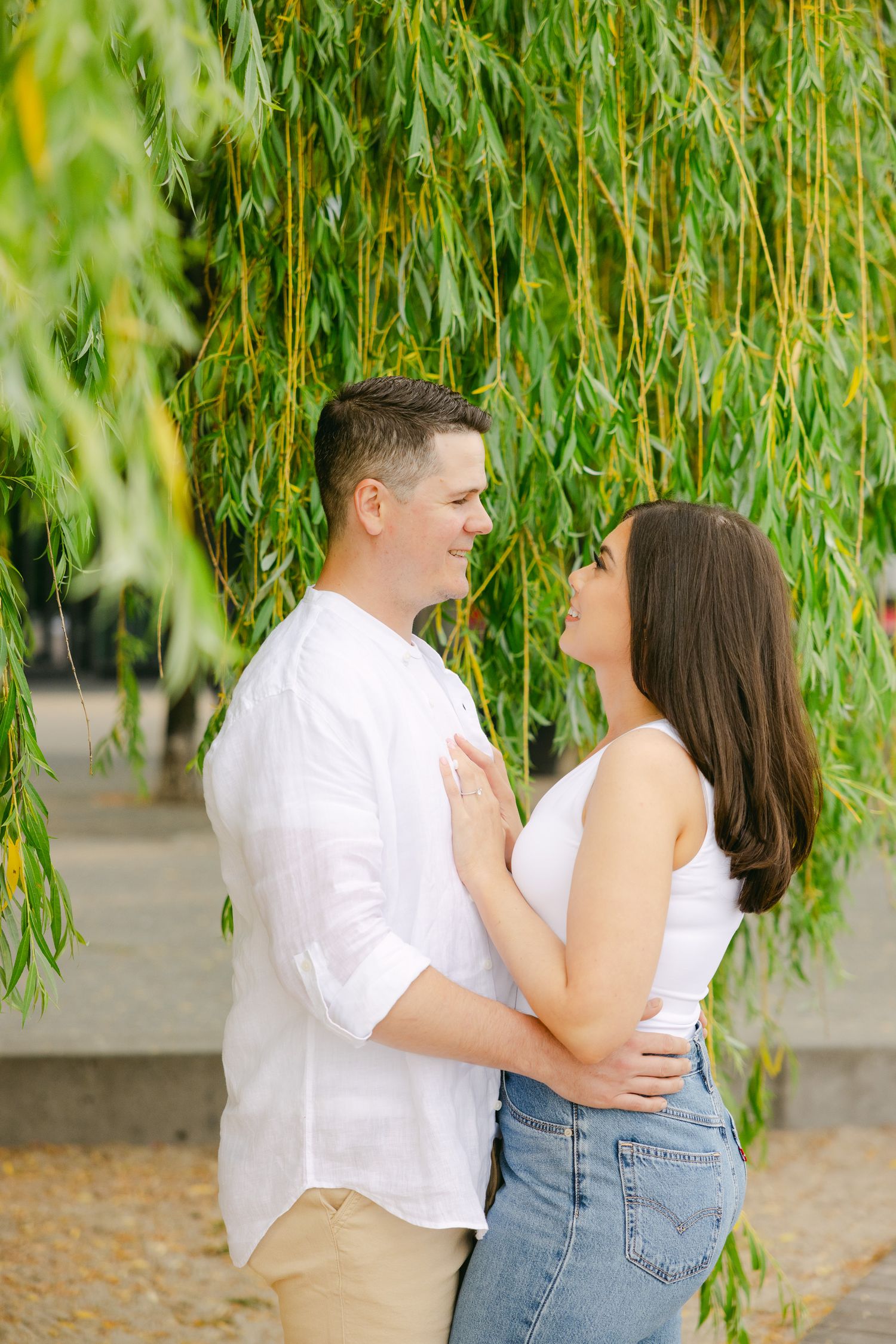 Intimate couple portrait under hanging willow branches by waterfront.
