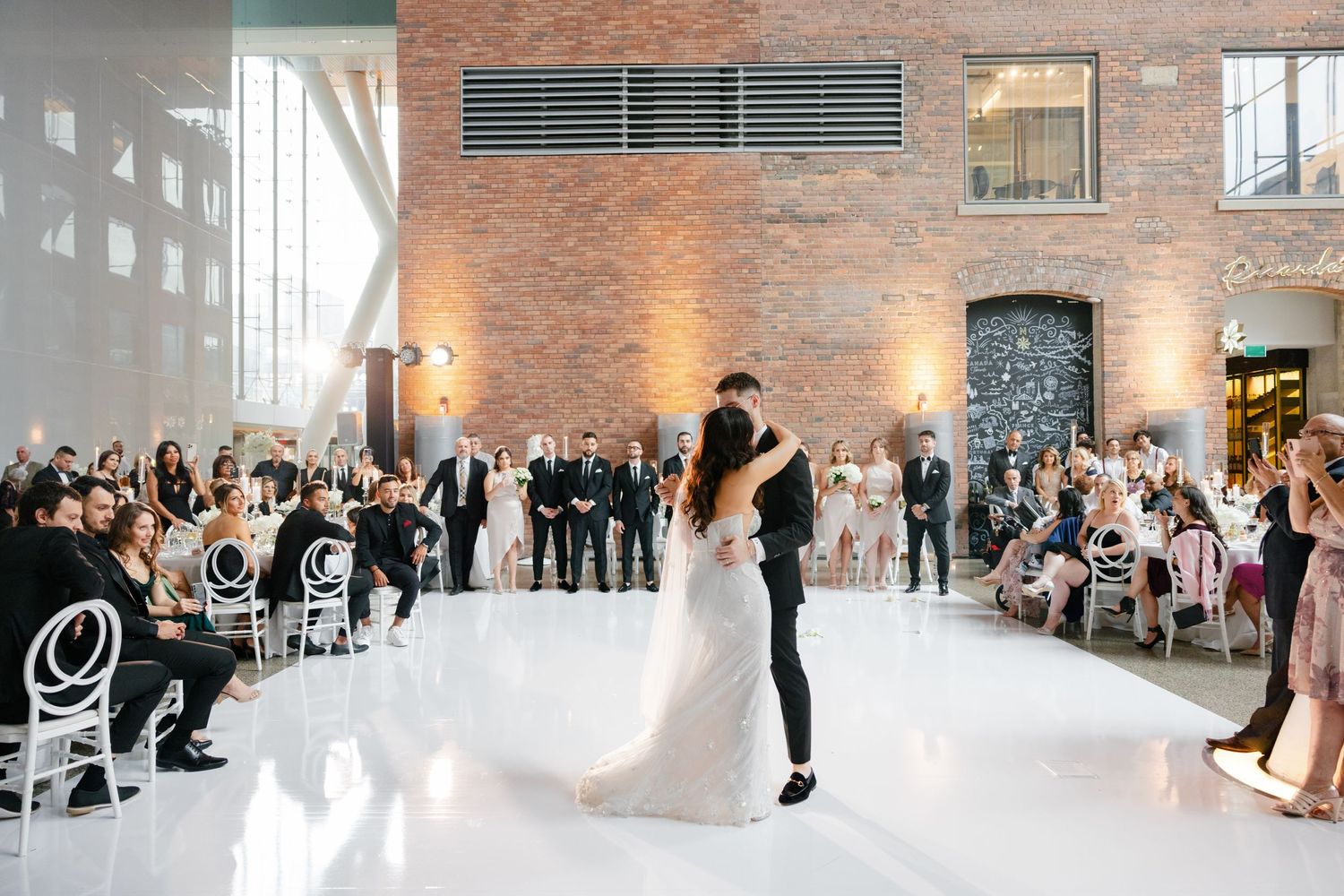 Couple sharing their first dance at a modern wedding reception with brick walls and elegant white decor.