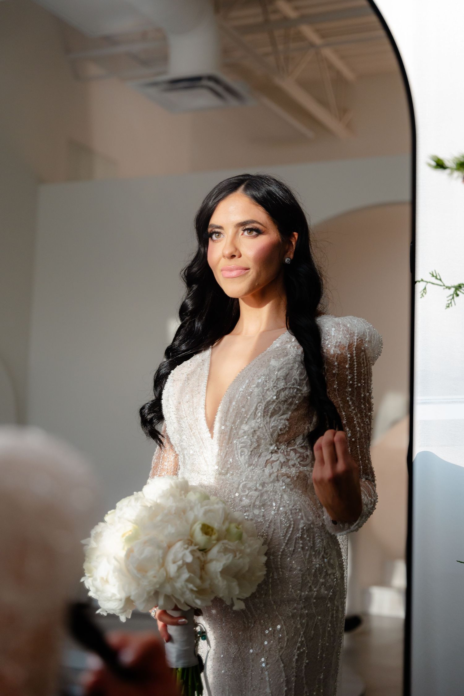 Bride in sparkly v-neck dress holds white bouquet while posing in natural light.