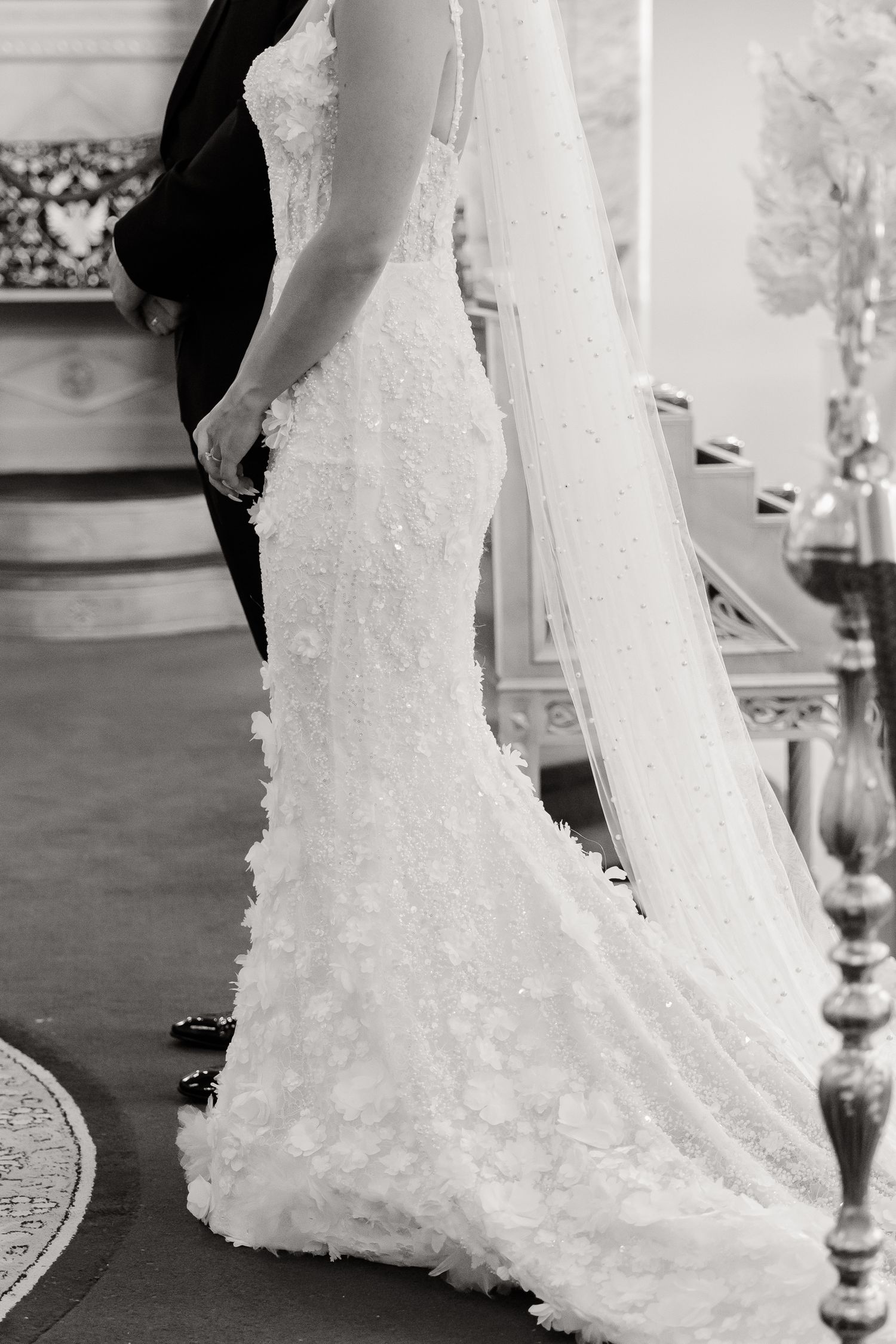 Close-up black and white view of an elegant lace wedding dress with delicate floral details and flowing train.