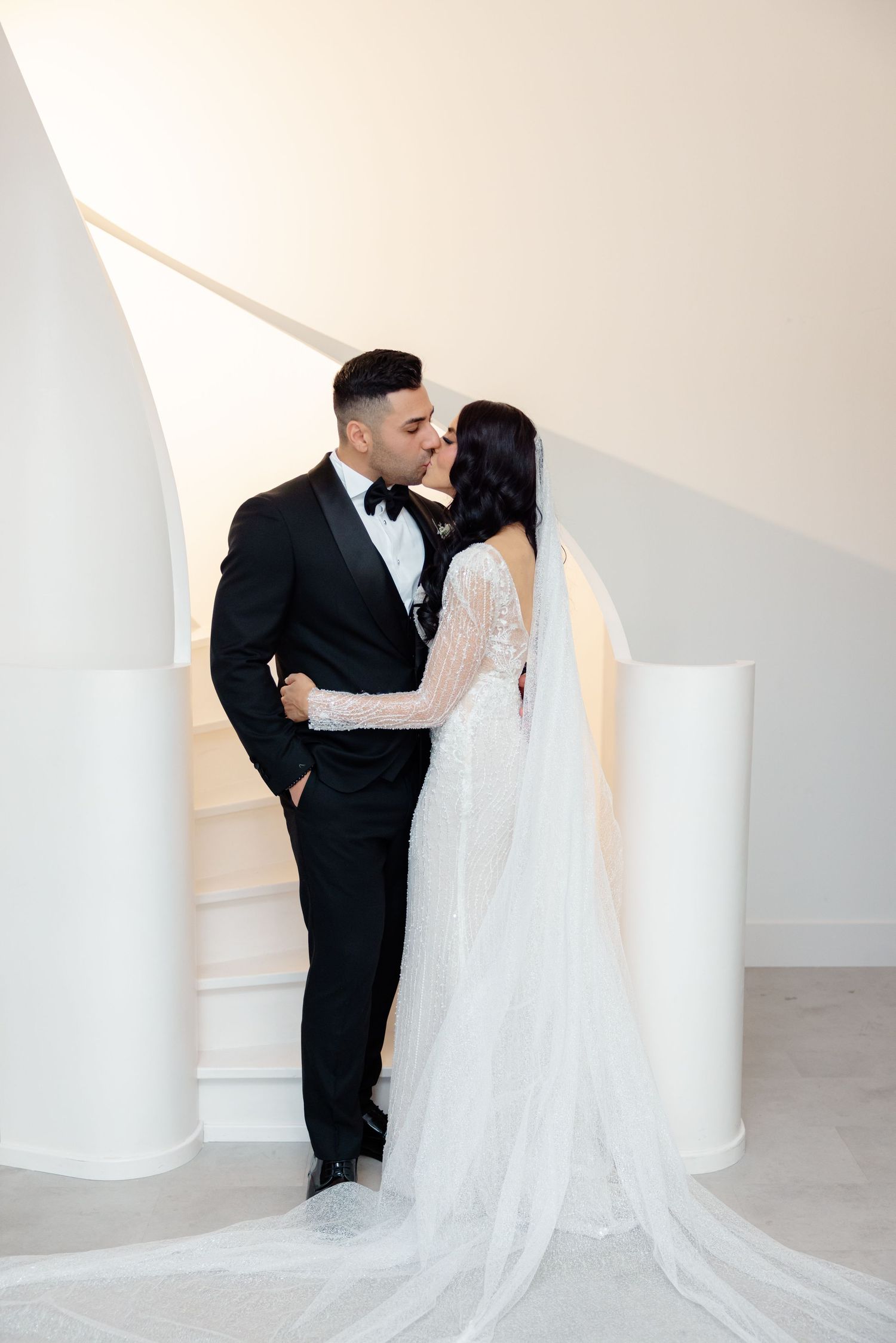 Wedding couple sharing an intimate moment against white architectural backdrop.