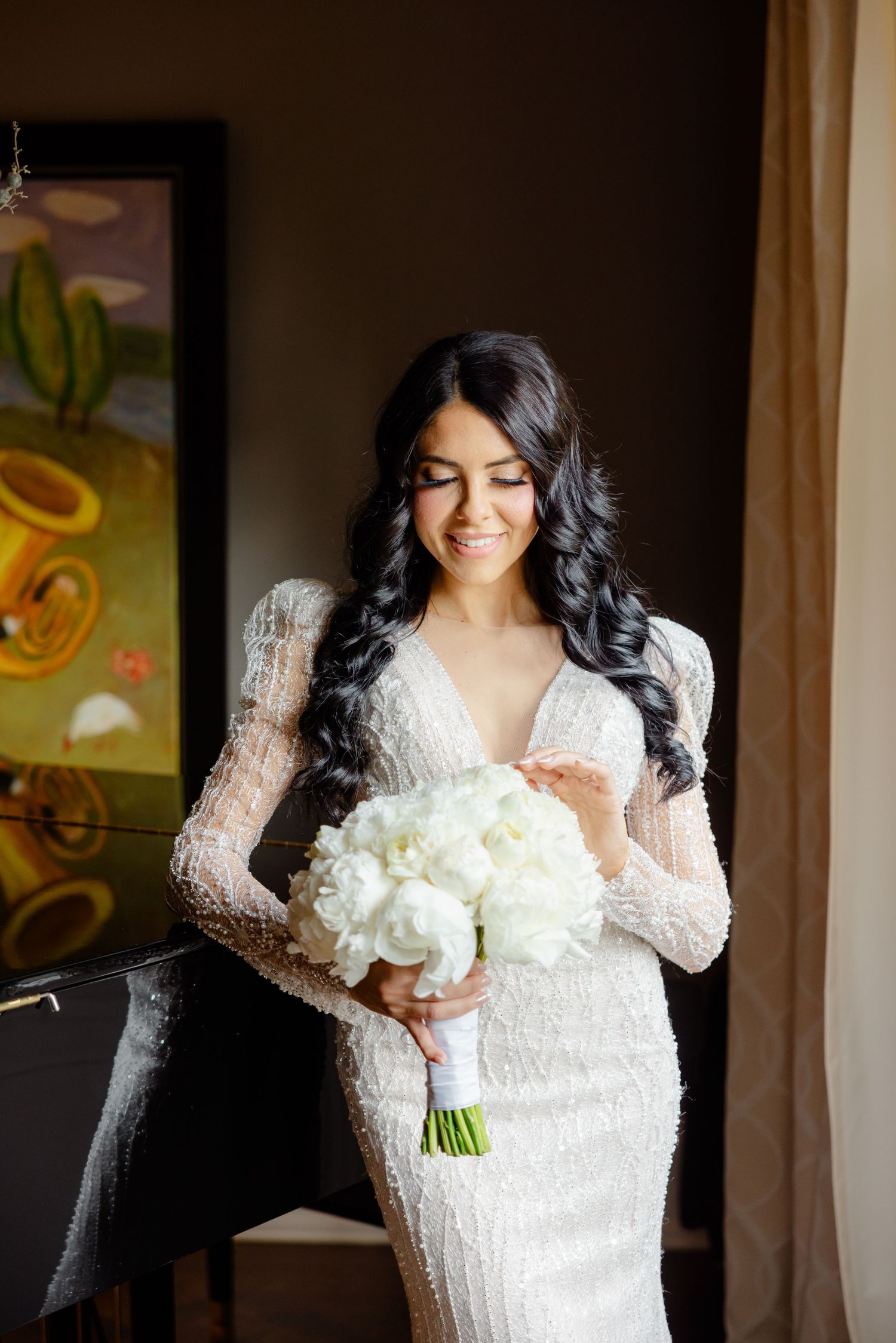 Beautiful bridal portrait featuring long-sleeved lace gown and white bouquet indoors.
