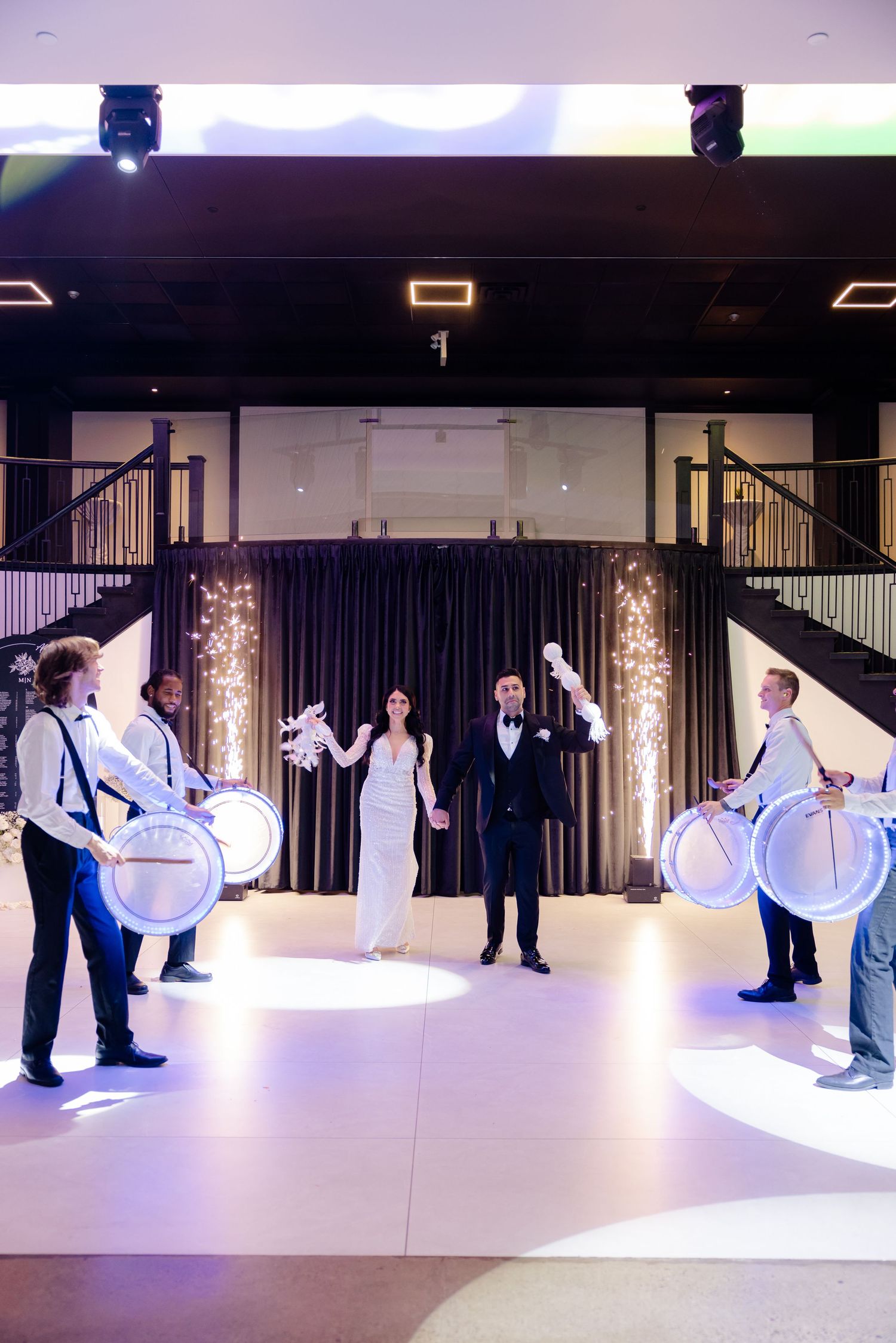 Wedding celebration with traditional drummers performing in an elegantly lit venue space.