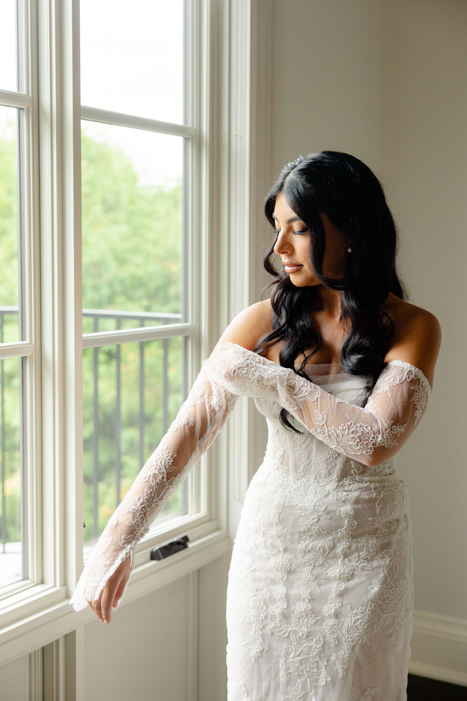 Elegant lace wedding dress with delicate long sleeves showcased in a bright room with natural window light.