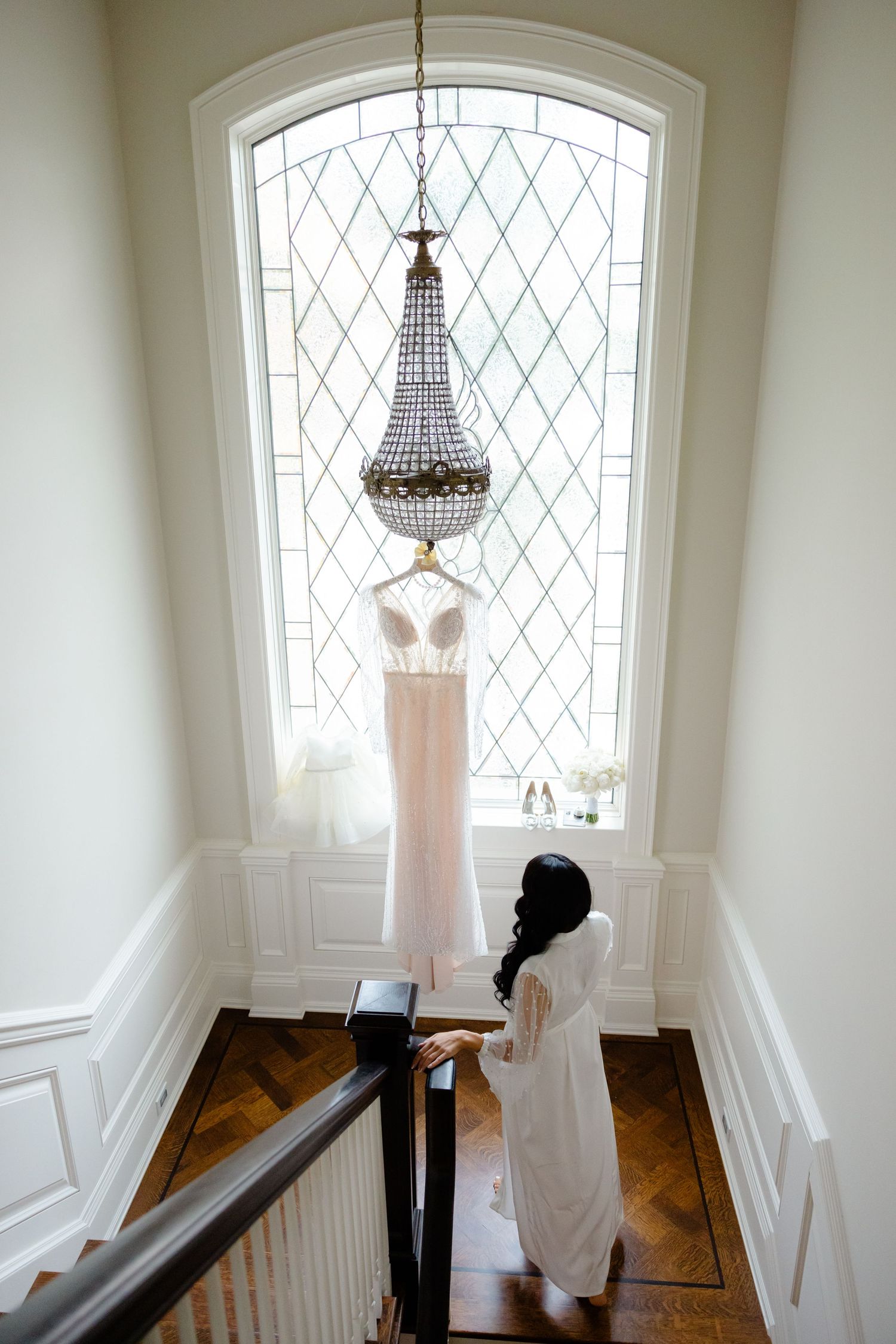Elegant wedding dress displayed in arched window alcove with crystal chandelier.