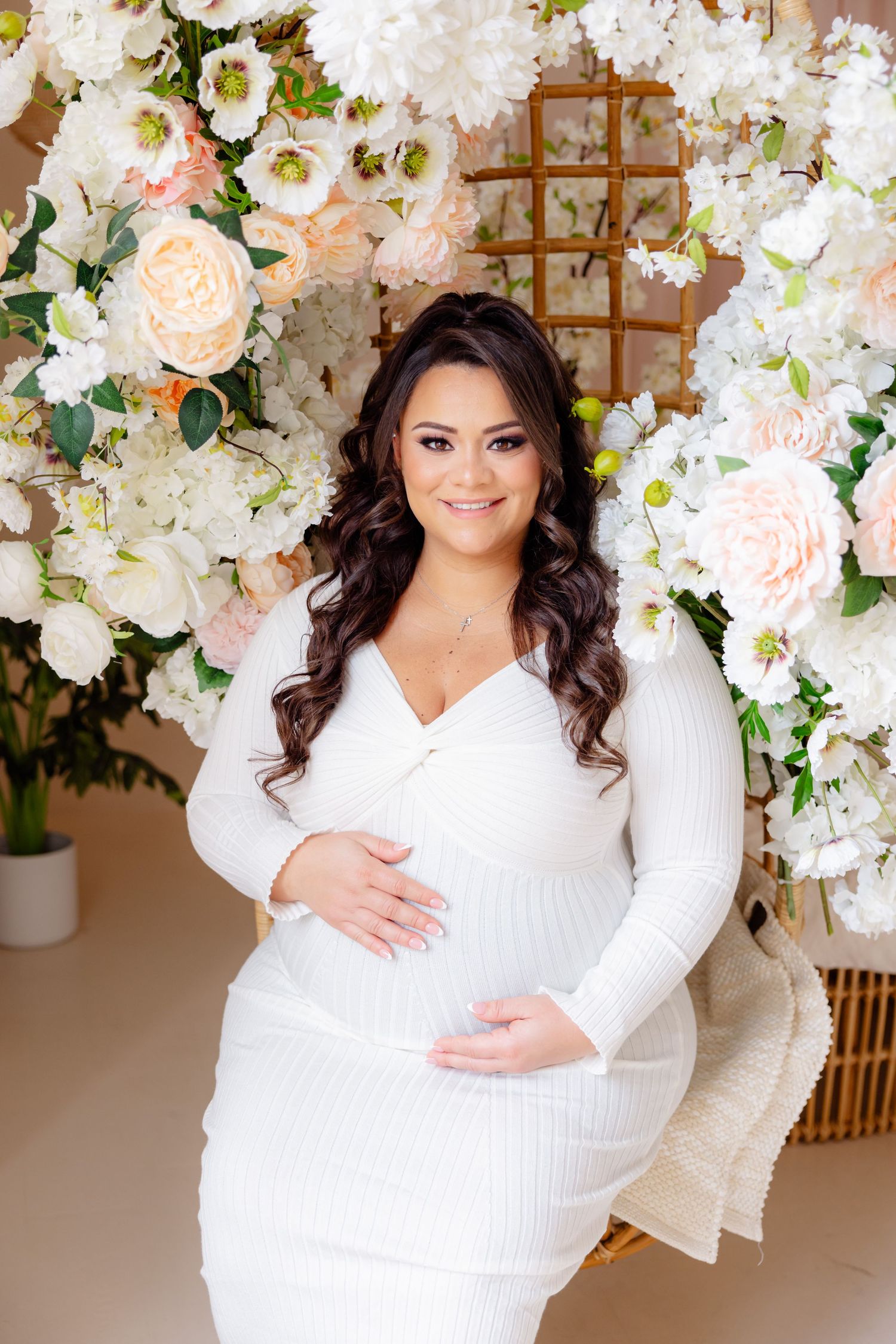 Elegant white maternity gown photographed against a floral backdrop with white and peach roses.