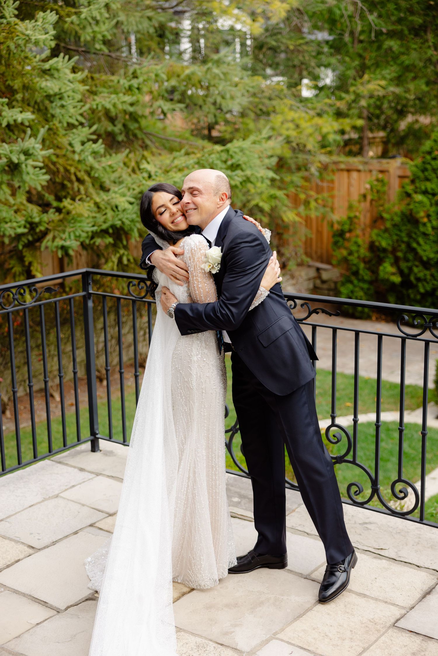 Joyful wedding couple embracing and laughing on an outdoor terrace with autumn trees.
