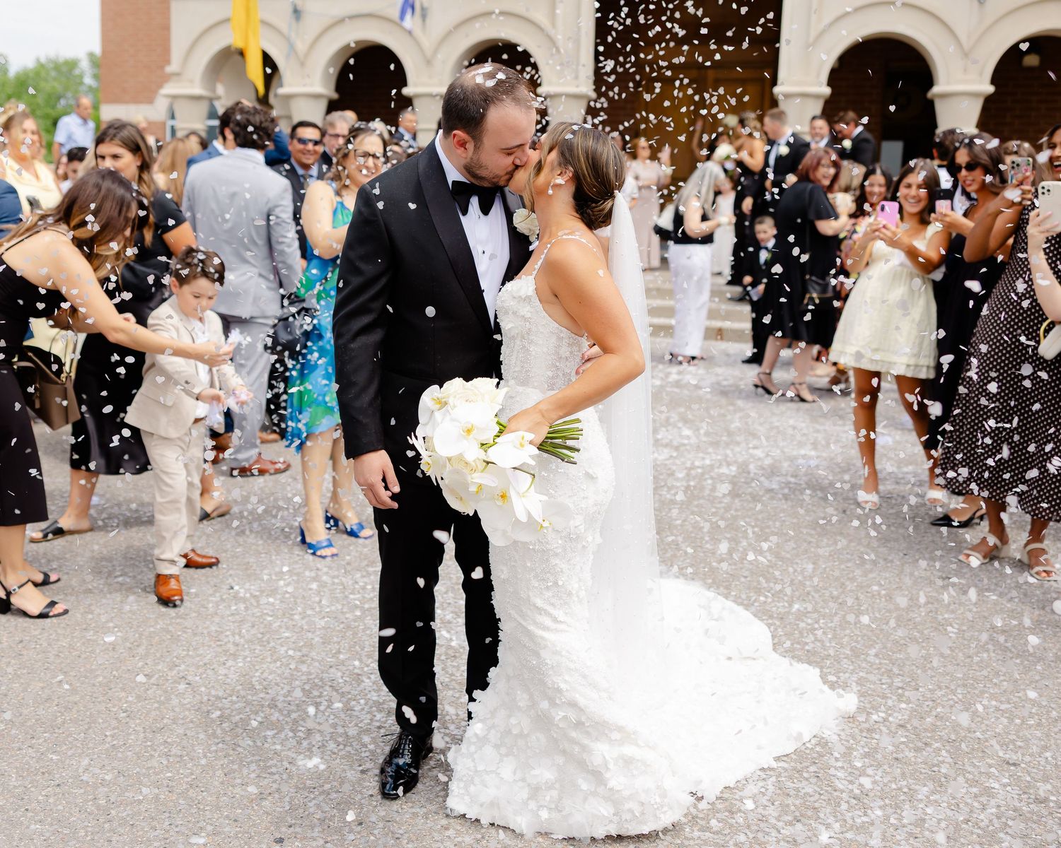 Wedding couple exits ceremony while guests toss white confetti on a beautiful celebration day.