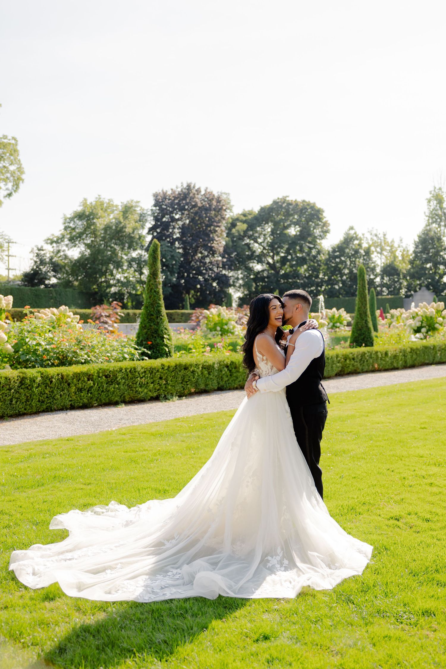 A romantic wedding portrait in a manicured garden with the bride's dress trailing on green grass.