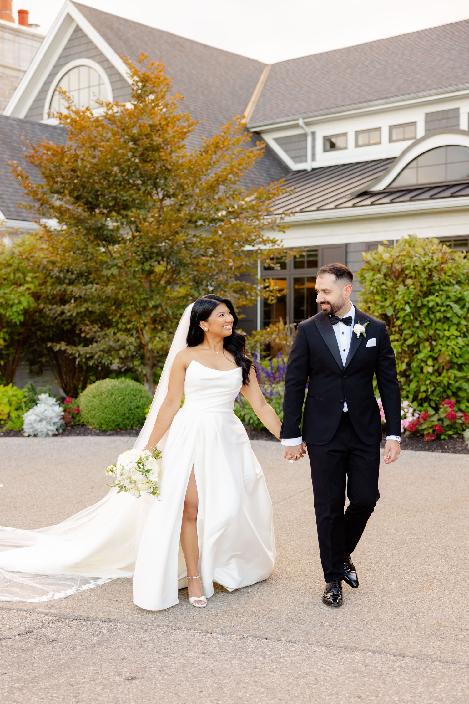 A bride in a flowing dress walks with her groom outside an elegant venue.