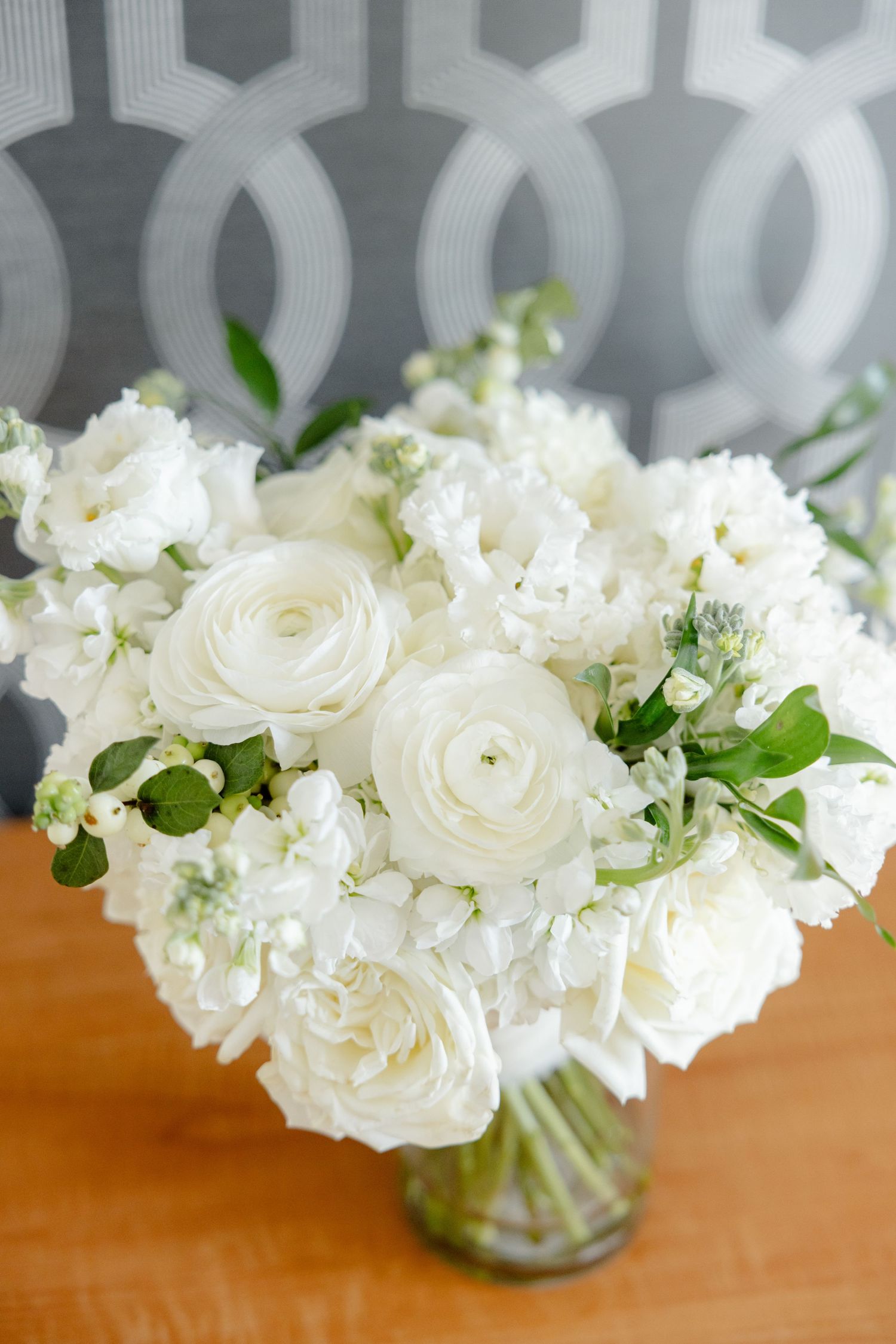 Fresh white rose and hydrangea bouquet arranged in glass vase against gray patterned background.