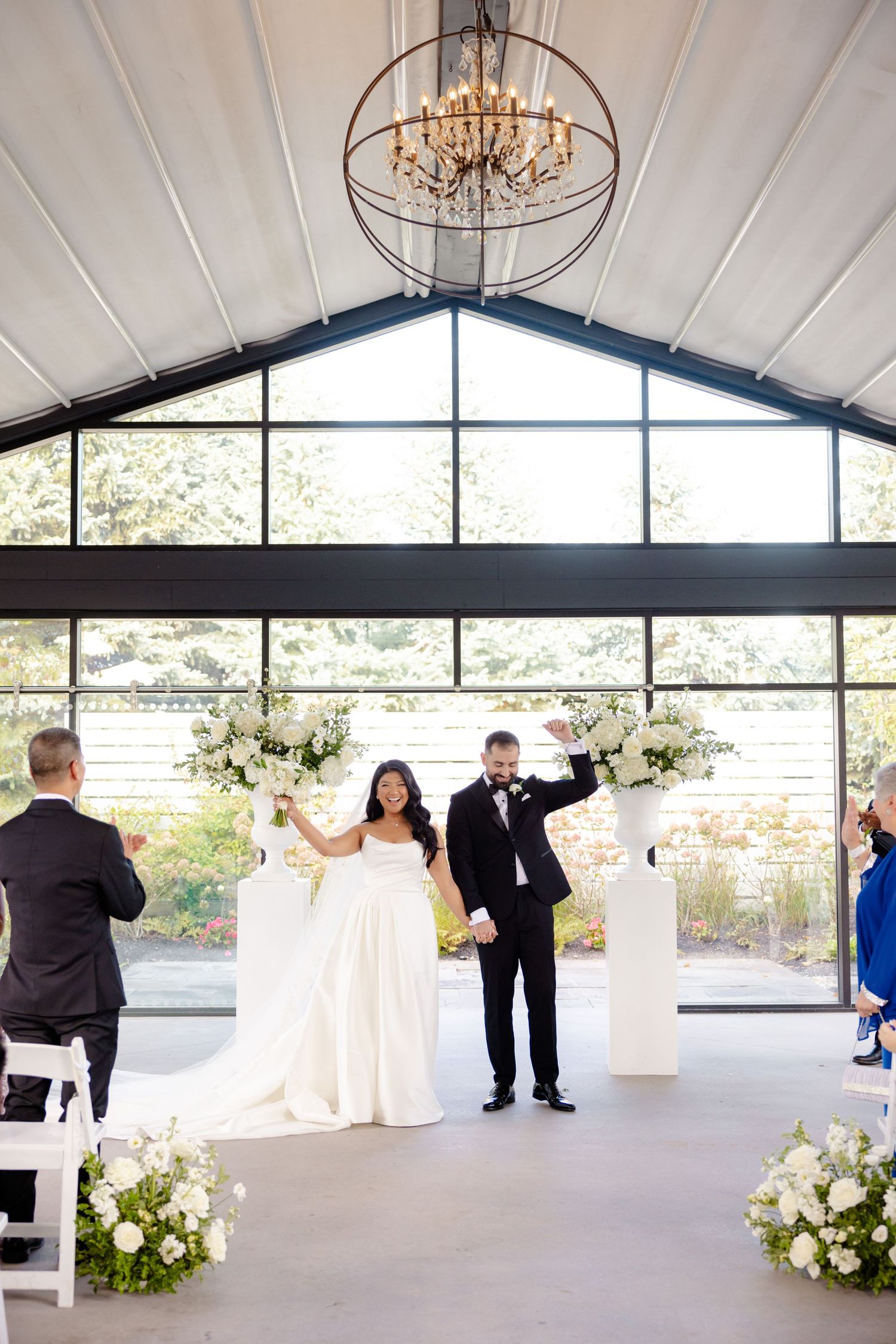 Wedding couple celebrates their marriage in a modern venue with chandelier and floral pedestals.