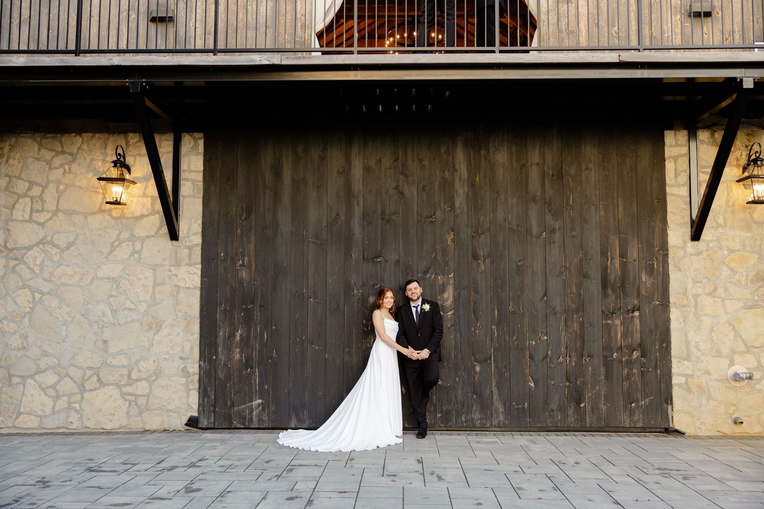 Wide architectural wedding shot featuring rustic wooden wall and stone facade.