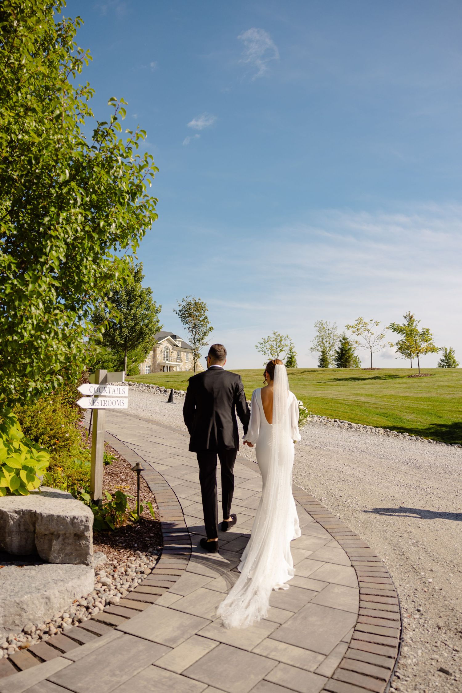 Couple walking down a curved stone path on their wedding day with scenic landscape in background.