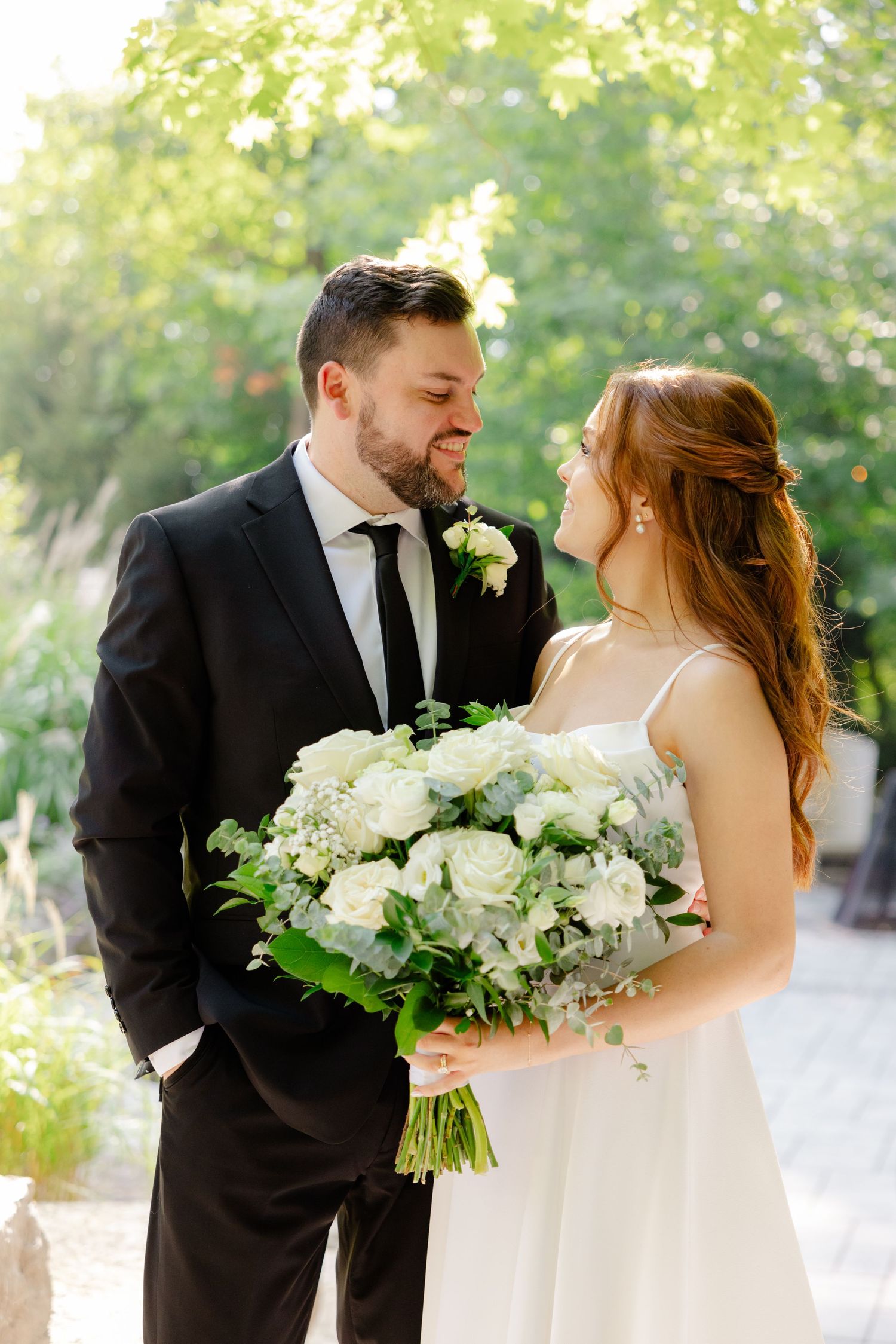 A tender wedding moment between newlyweds sharing laughter amidst green foliage.