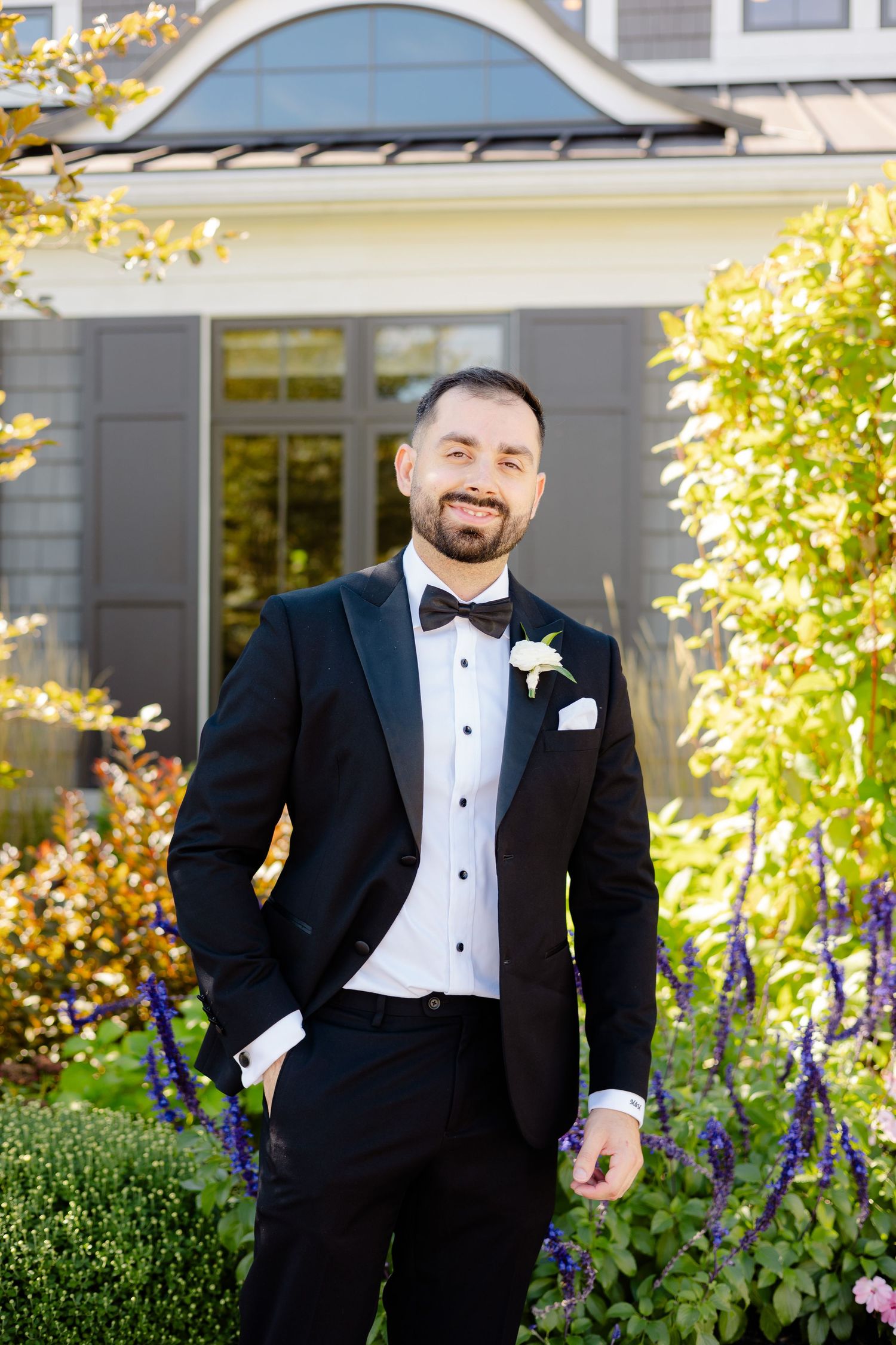 Classic wedding portrait of groom in tuxedo with boutonniere against yellow autumn foliage.