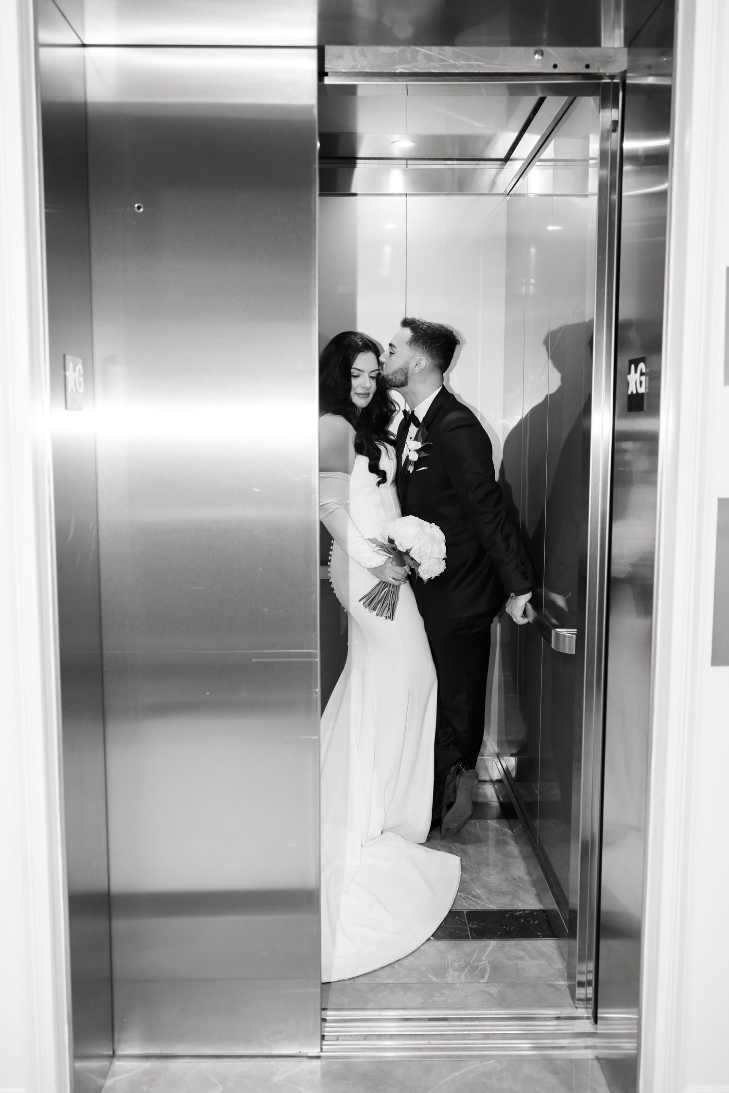 Black and white wedding photograph of couple sharing intimate moment in elevator.