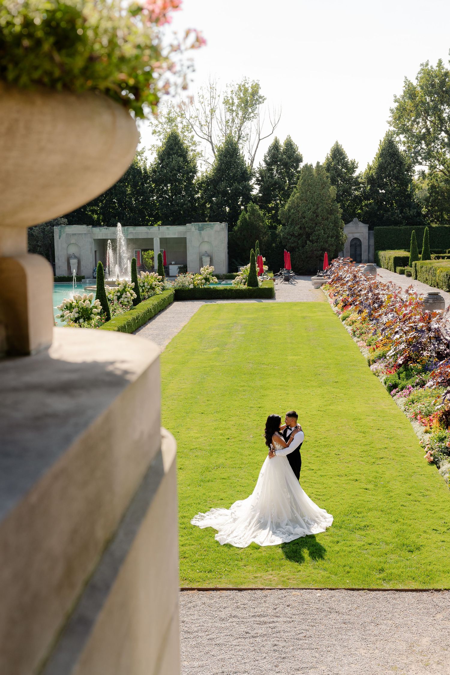 A couple dances on a pristine lawn surrounded by formal gardens viewed from above.