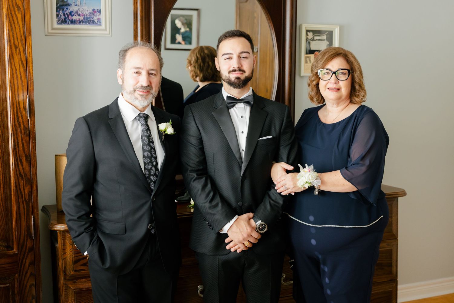 Three people in formal attire stand together for a family wedding photo in an elegant indoor setting.