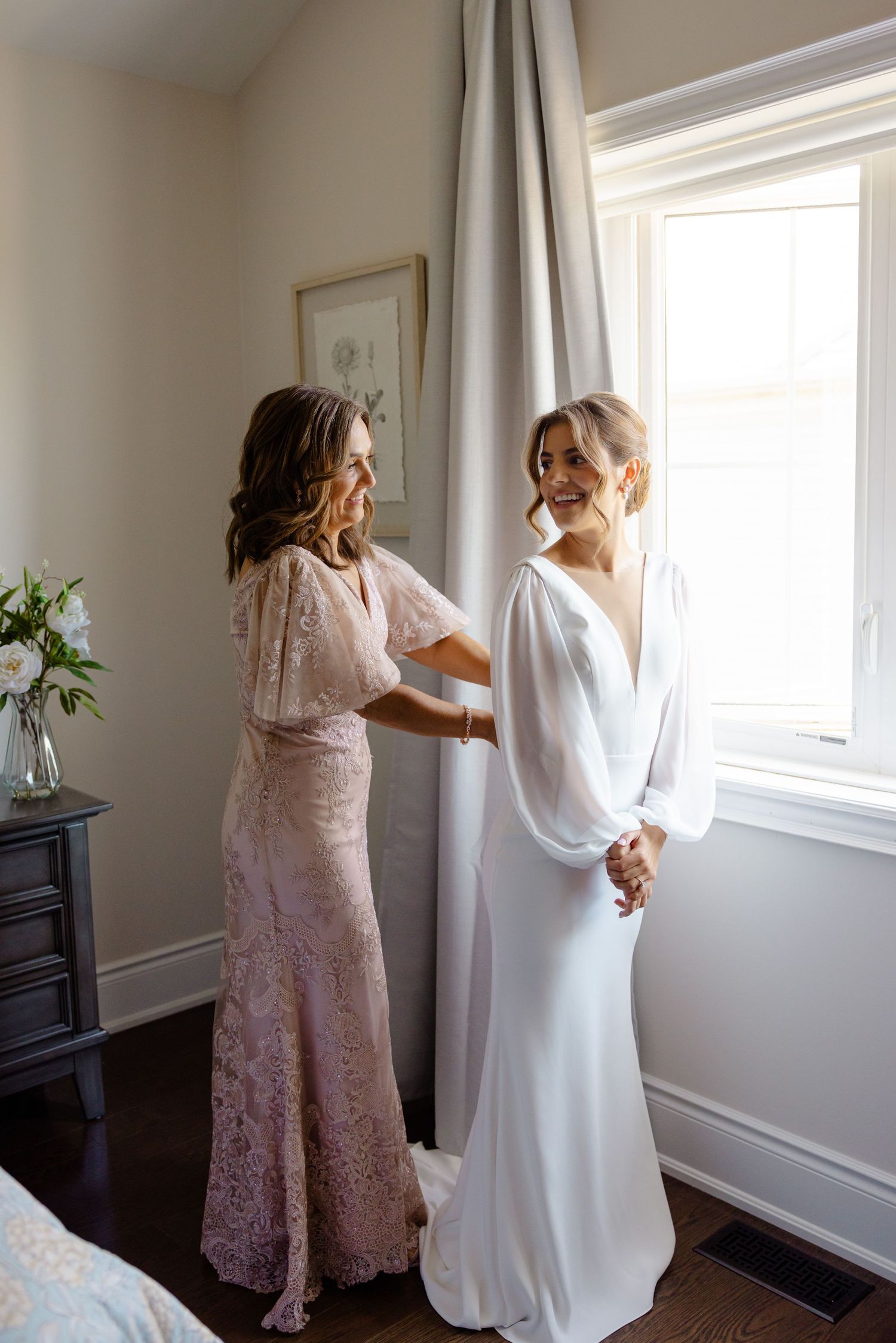 Two people in formal attire share a touching moment by a bright window.