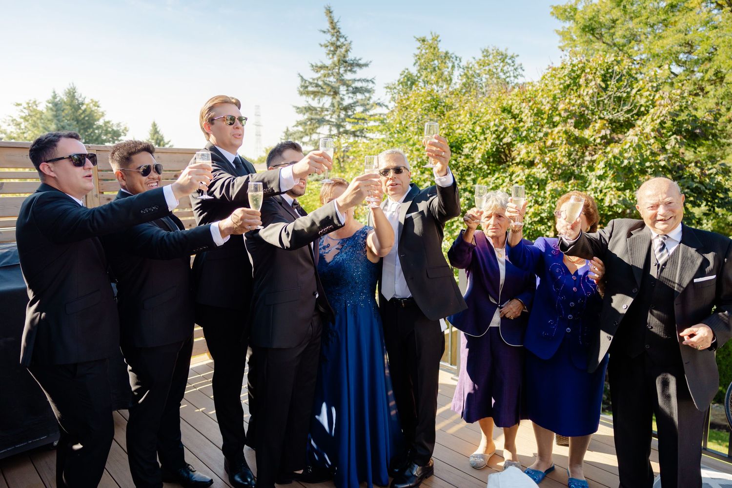 Joyful wedding party members raising drinks in unison during outdoor celebration.