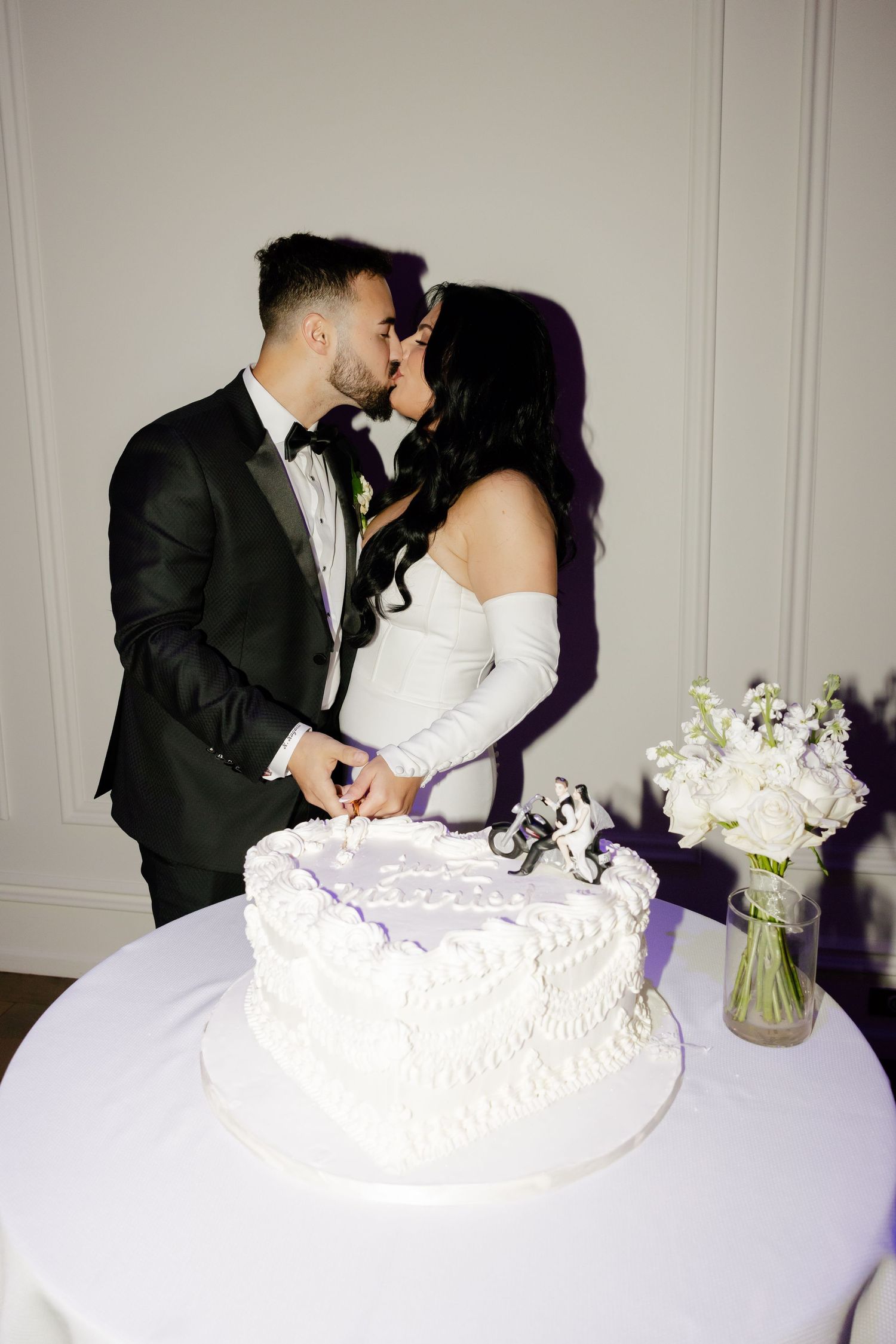 A romantic wedding cake cutting moment with a white tiered cake and floral bouquet on display.