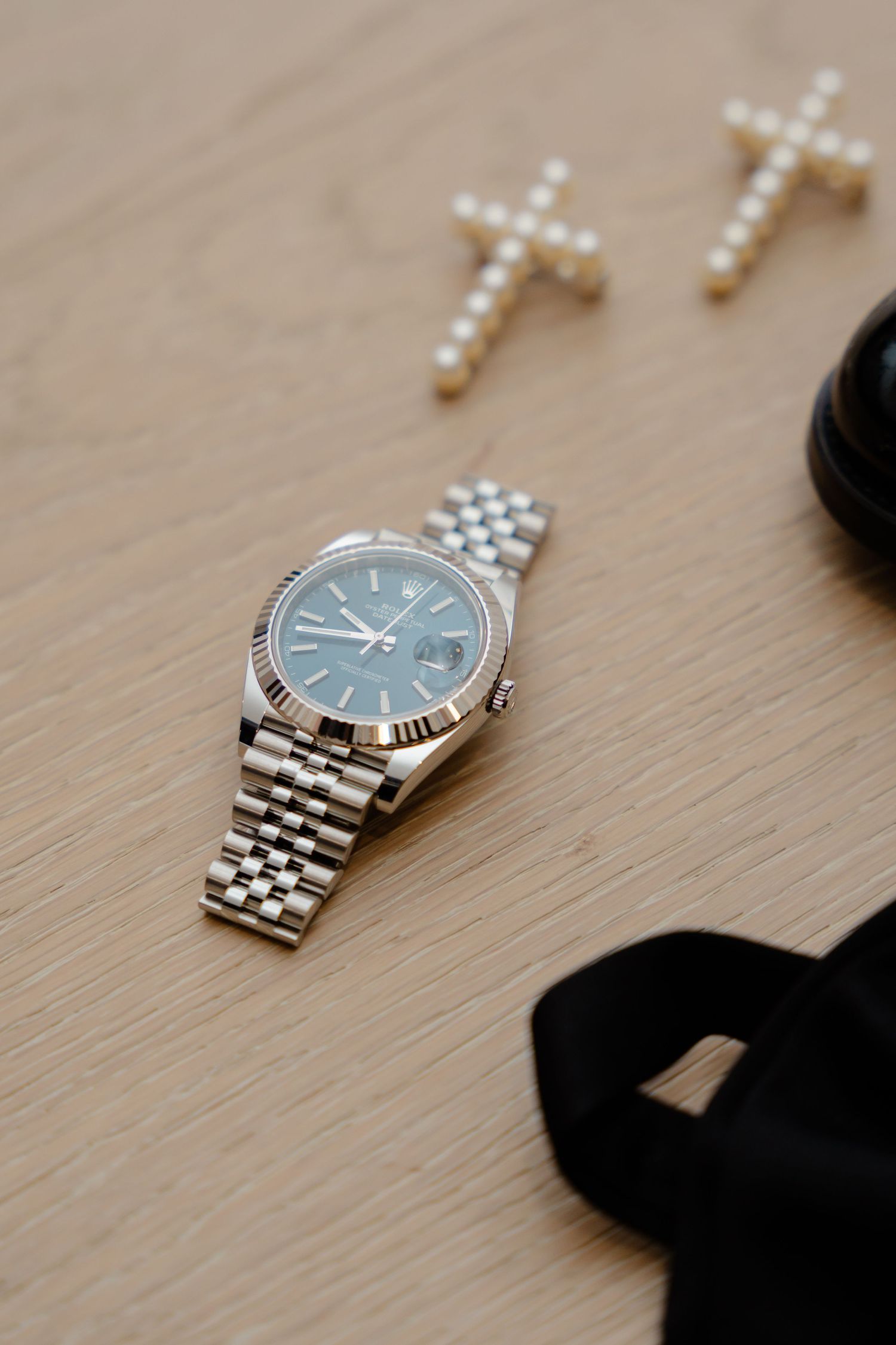 Luxury silver wristwatch with pearl cross accessories on wooden surface.