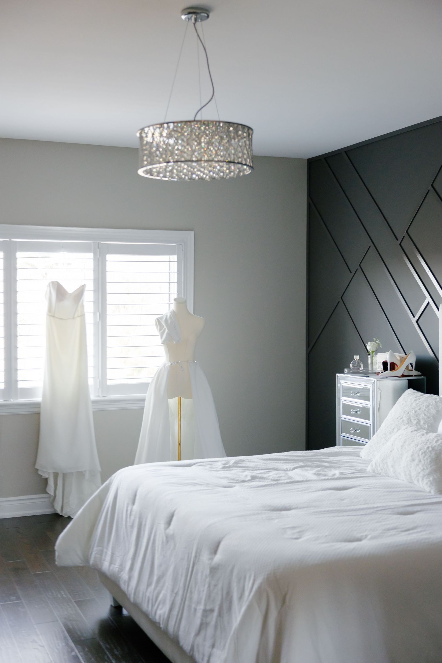 Modern bedroom with crystal chandelier featuring wedding dresses and dark geometric accent wall.