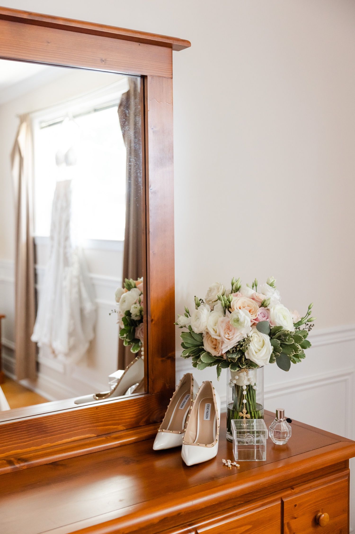 Elegant vanity setup with mirror, white heels and fresh floral arrangement in soft lighting.