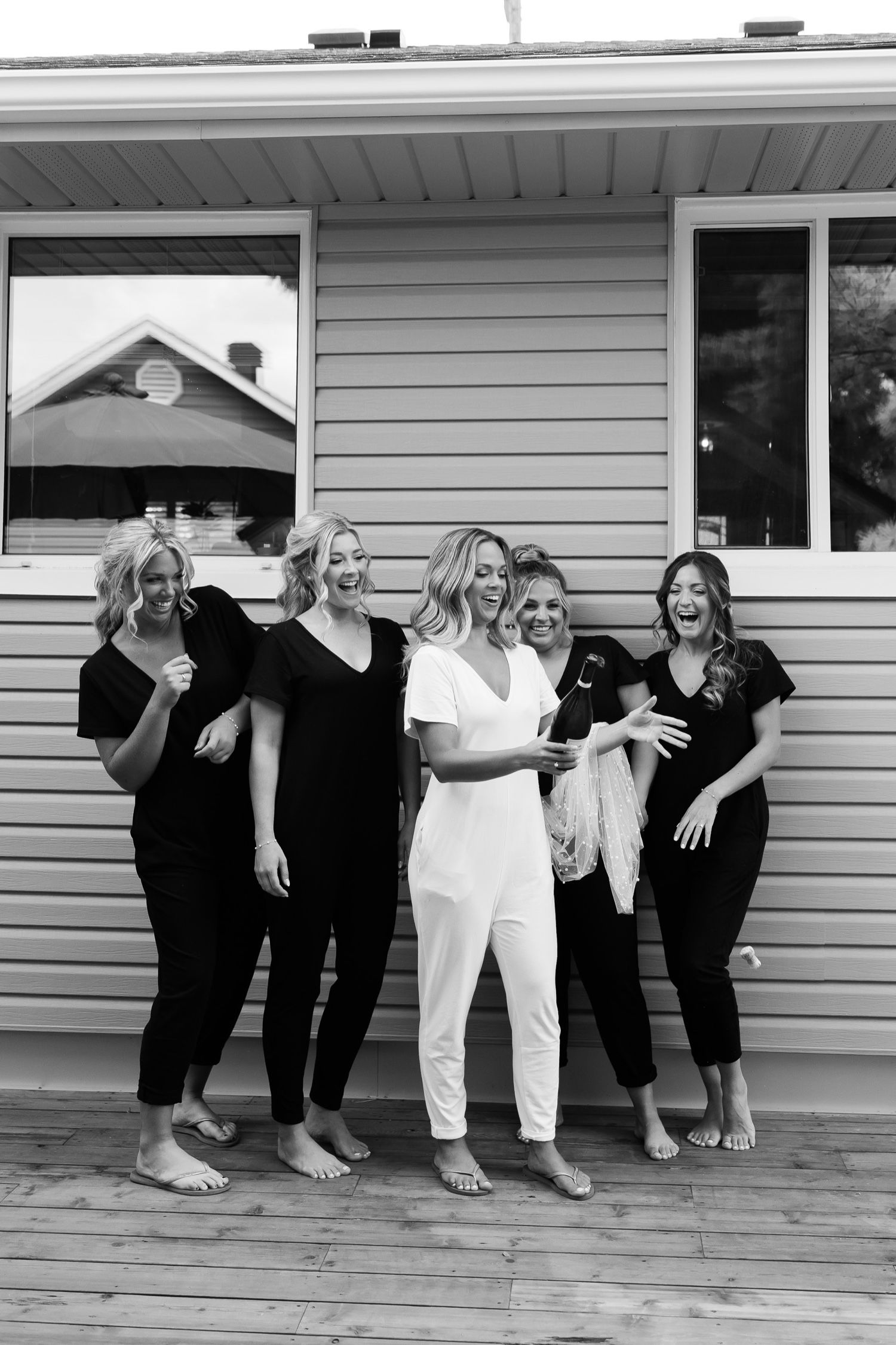 Group poses together on a deck outside a house, one in white surrounded by others in black.
