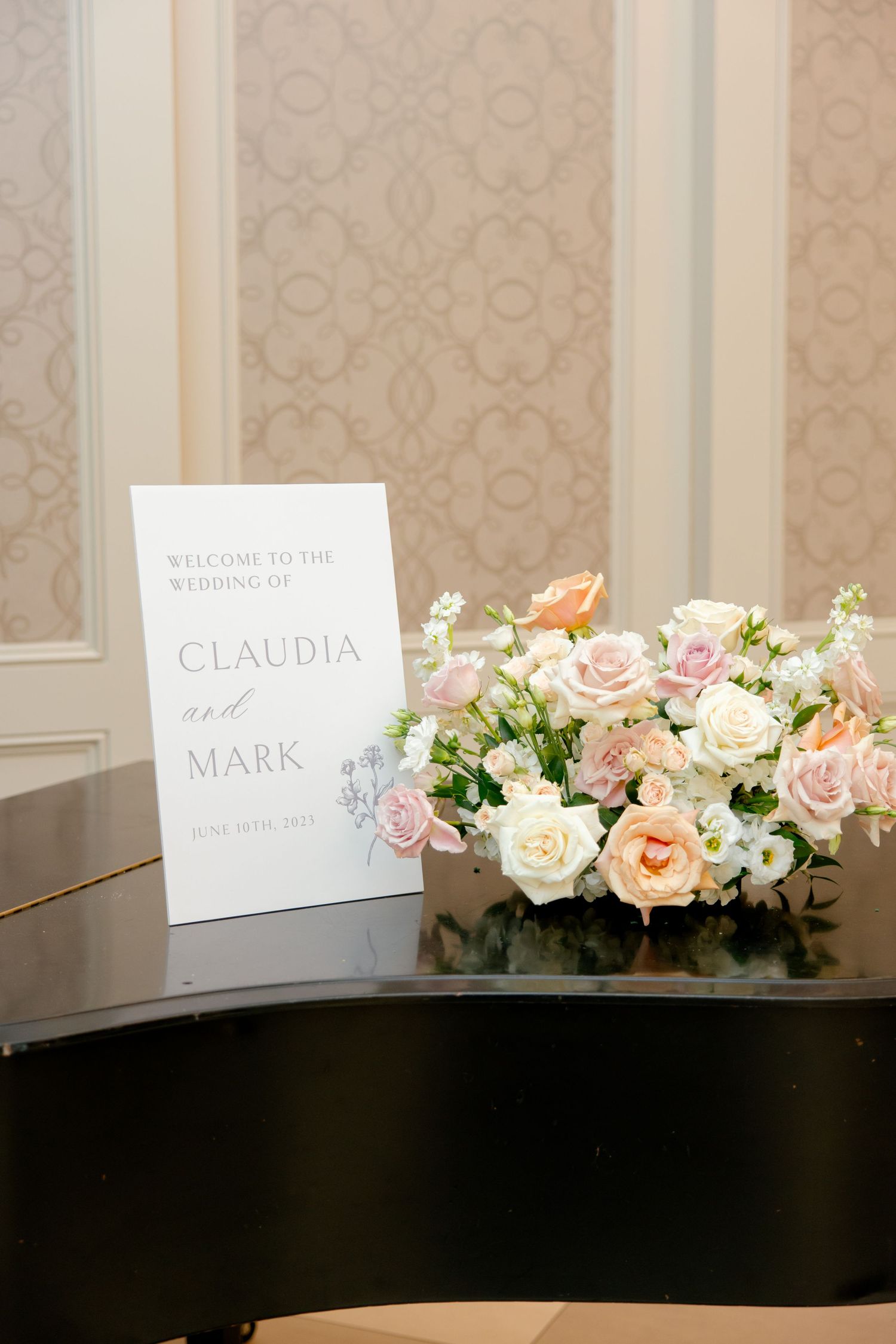 Wedding welcome sign and peach rose arrangement displayed on black piano.