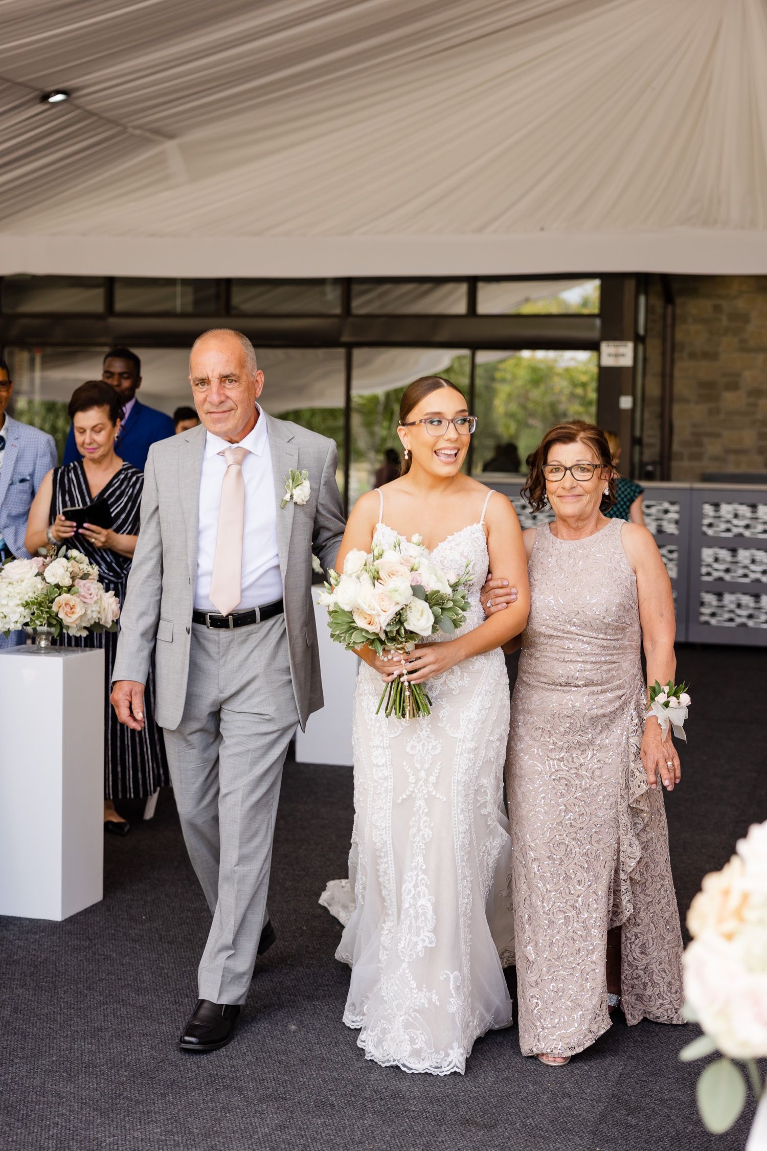 A formal processional moment at an elegant tented wedding ceremony with white floral decorations.